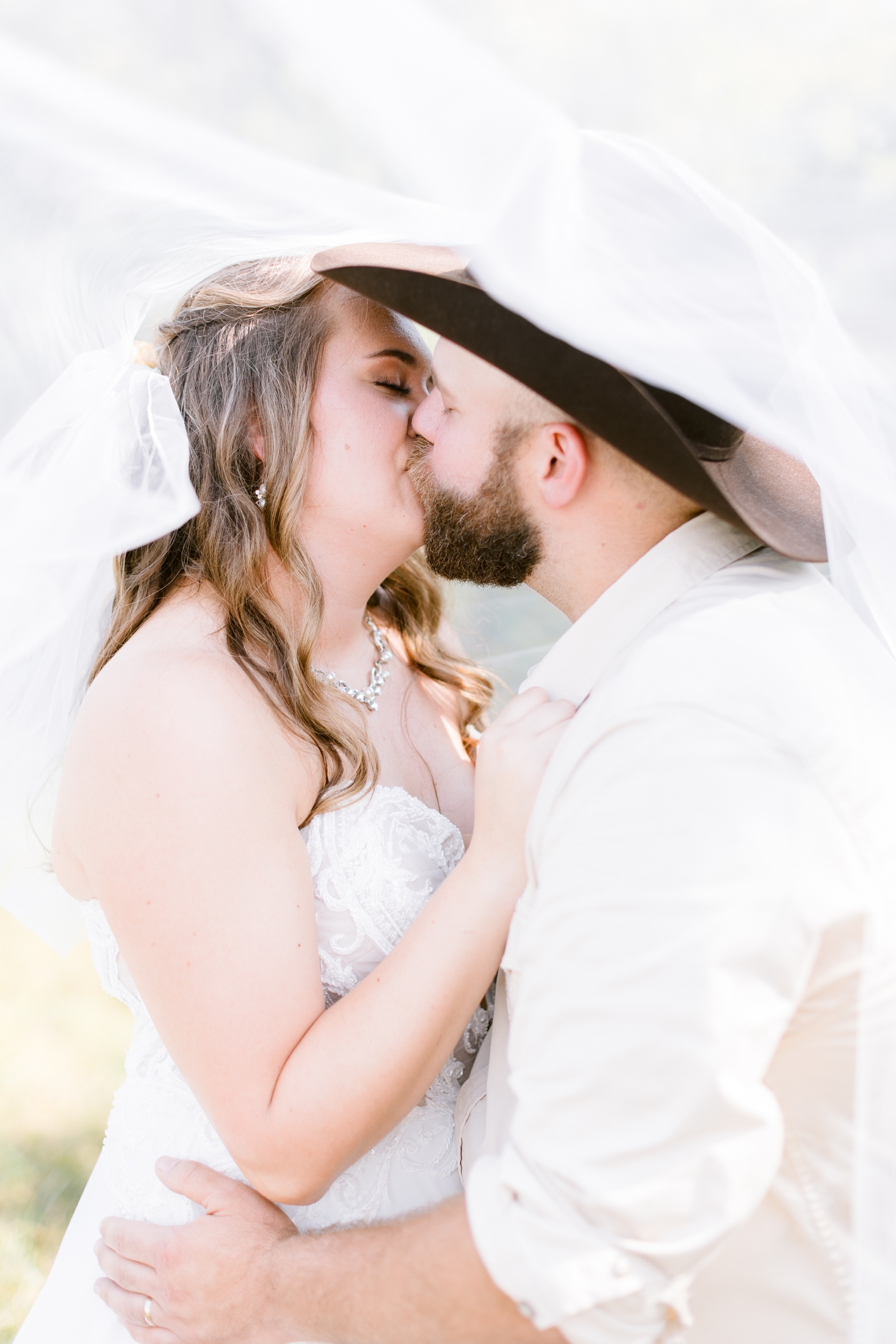 Megan and Matt share a kiss underneath her cathedral length veil | A rustic, country wedding with western touches | CB Studio