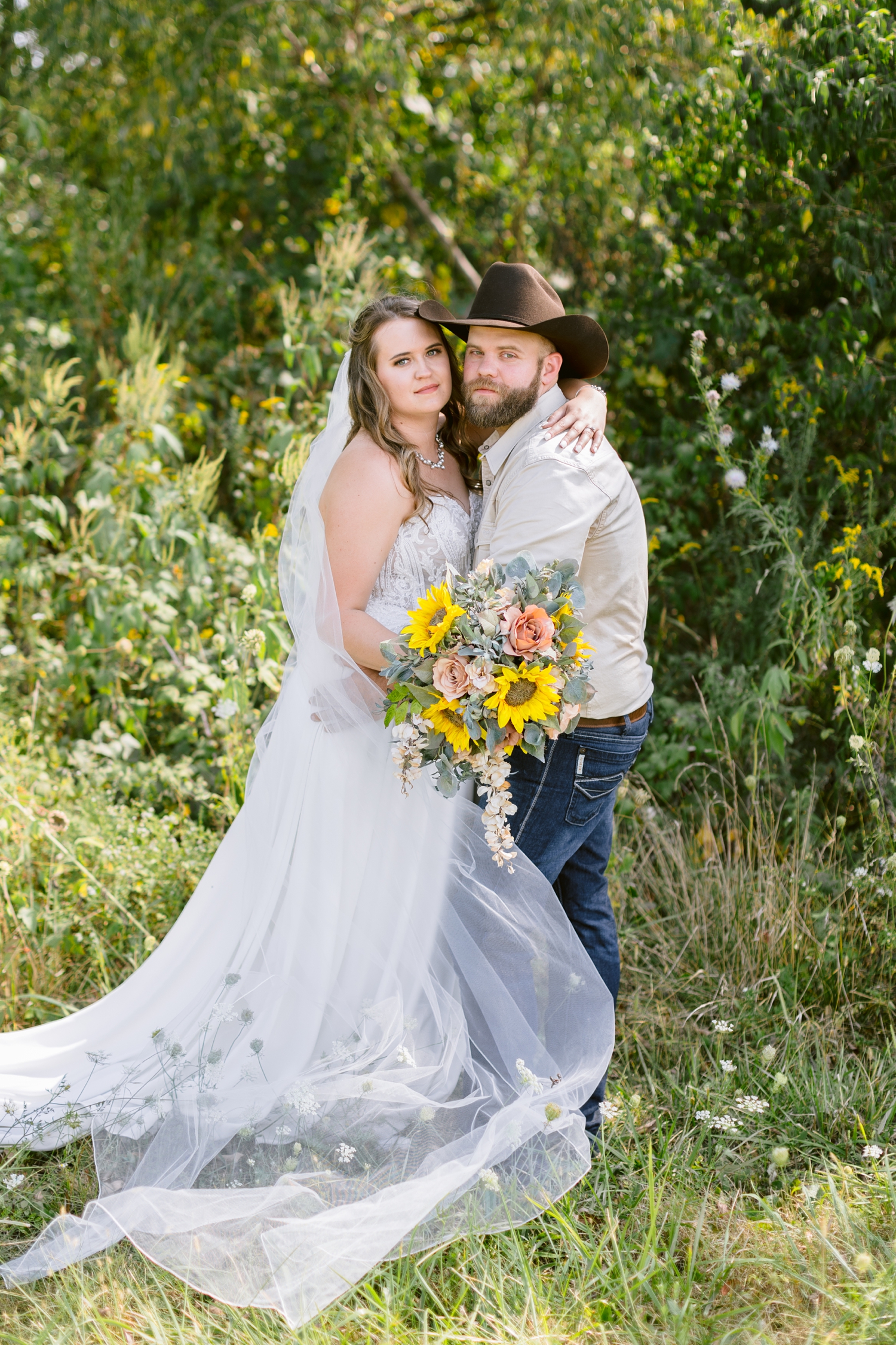 Megan and Matt embrace in a grassy, flower field in Knoxville, IA | A rustic, country wedding with western touches | CB Studio