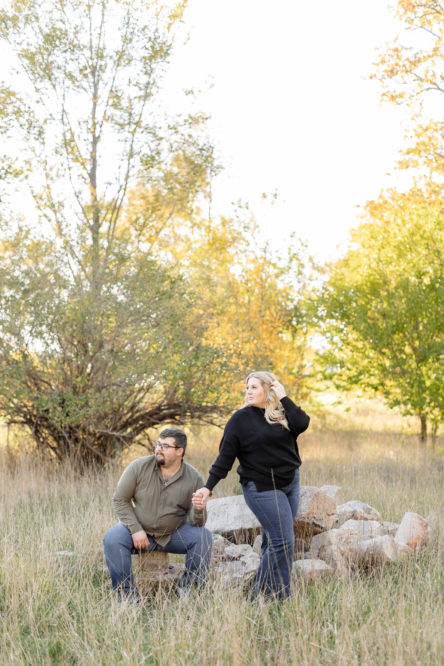 Nicks on a rock pile while Halie holds his hand as they look off in the distance in the middle of a grassy pasture | CB Studio