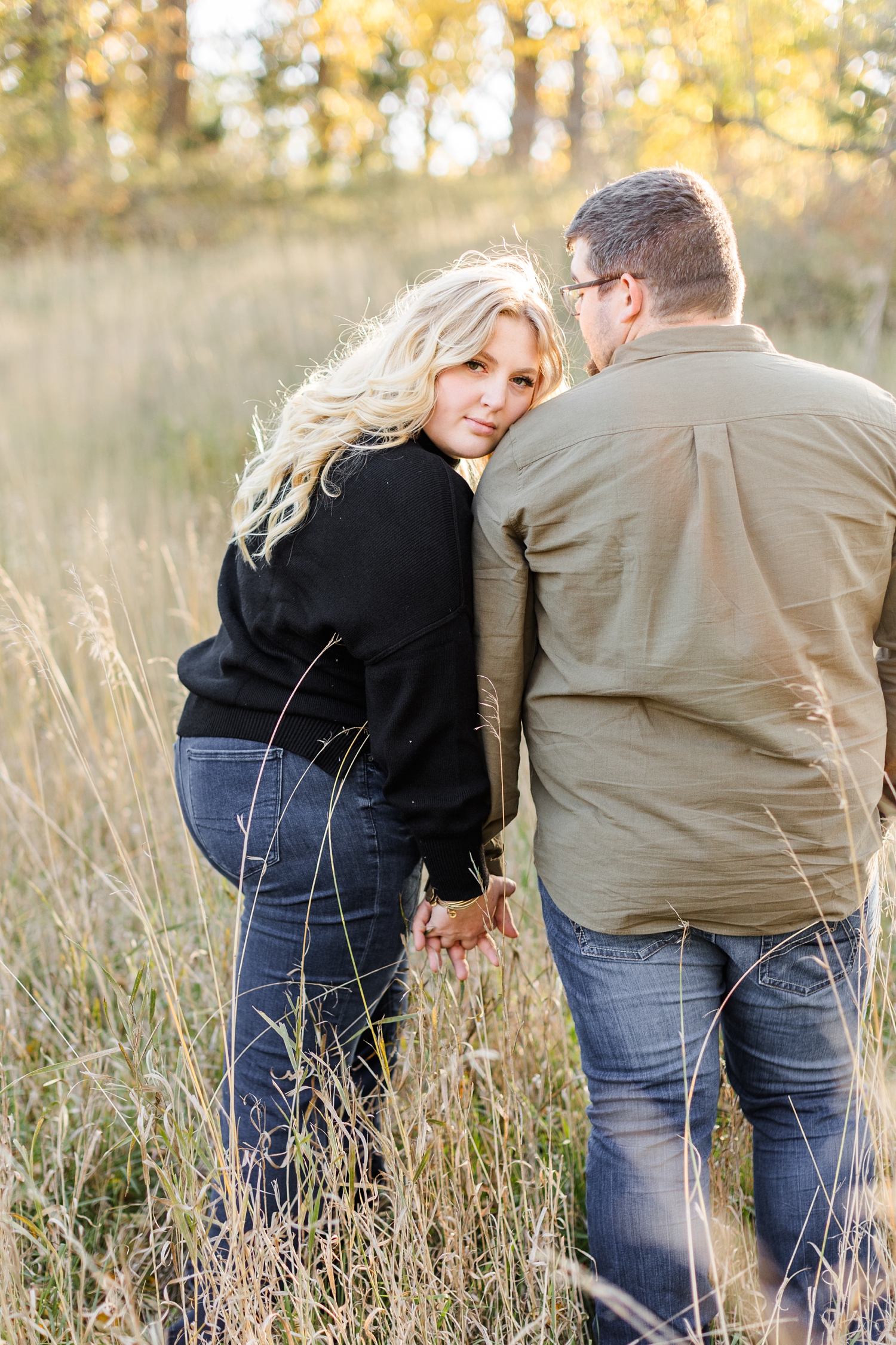 Halie leans her cheek against Nick's shoulder and looks back while Nick looks at her in the middle of a grassy pasture | CB Studio