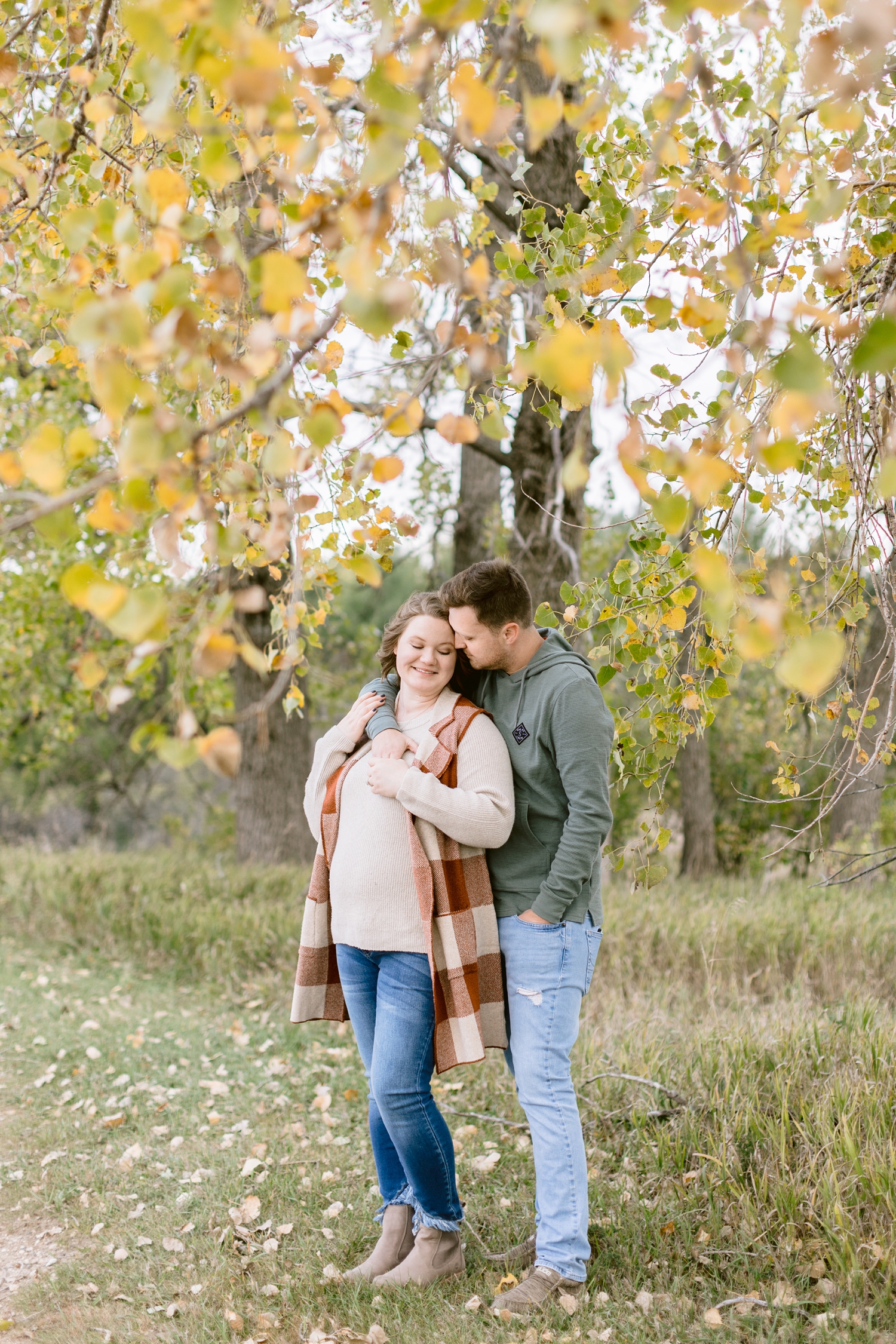 Justin and Kylie snuggle together under beautiful yellow fall leaves at Water's Edge Nature Center | CB Studio