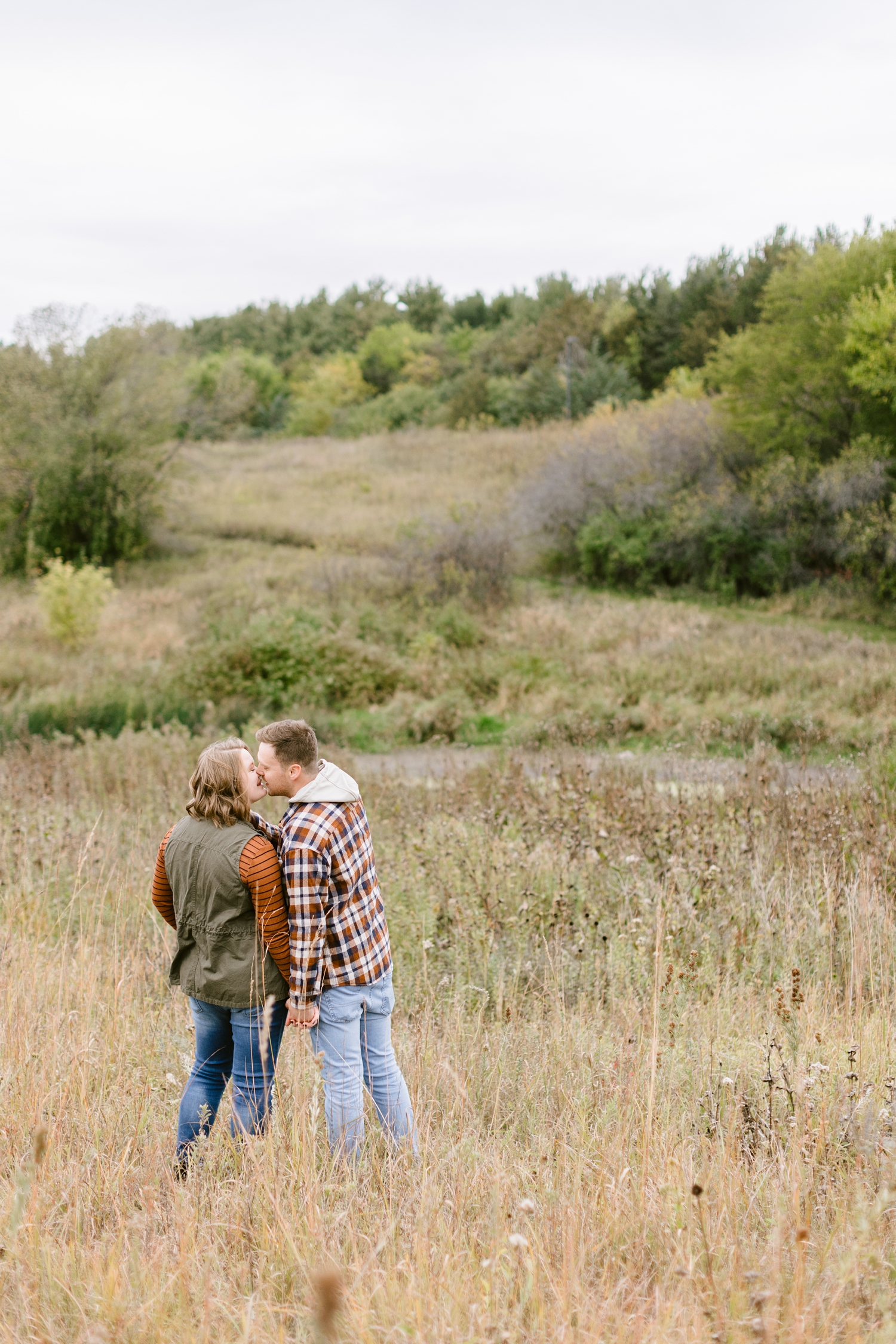 Justin and Kylie share a kiss together in the middle of a prairie grassy field at Water's Edge Nature Center | CB Studio