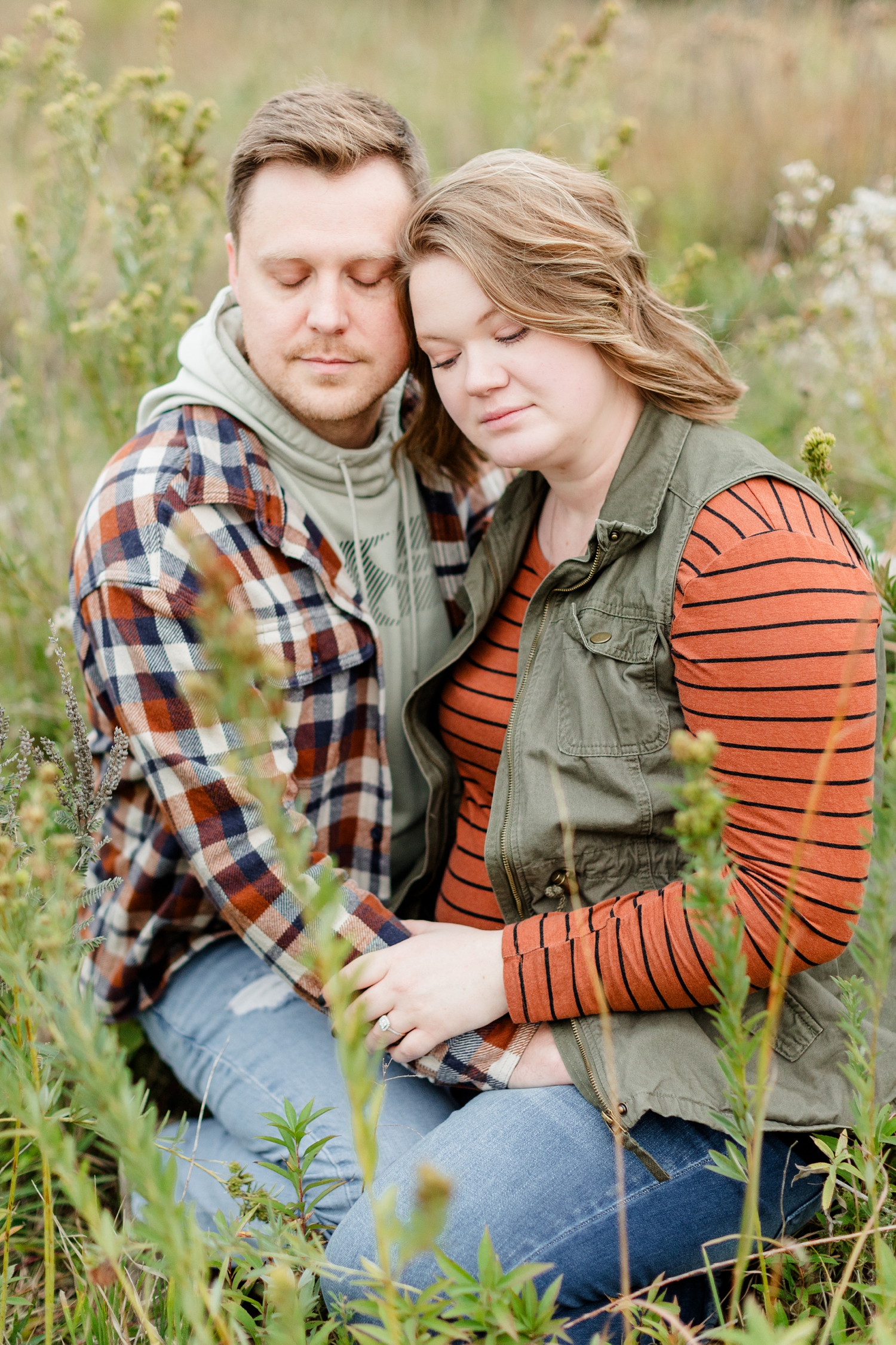 Justin and Kylie snuggle together as they squat in a prairie grassy field at Water's Edge Nature Center | CB Studio