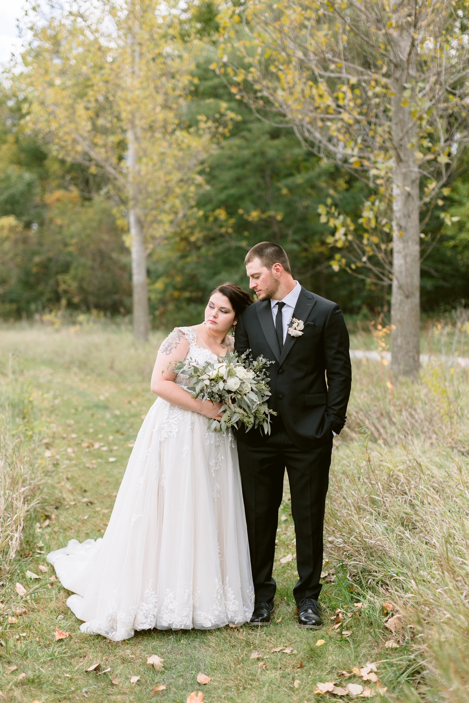 Mary leans her head on her new husband's shoulder as they stand surrounded by beautiful fall foliage at Sheldon Park, Humboldt, IA | CB Studio