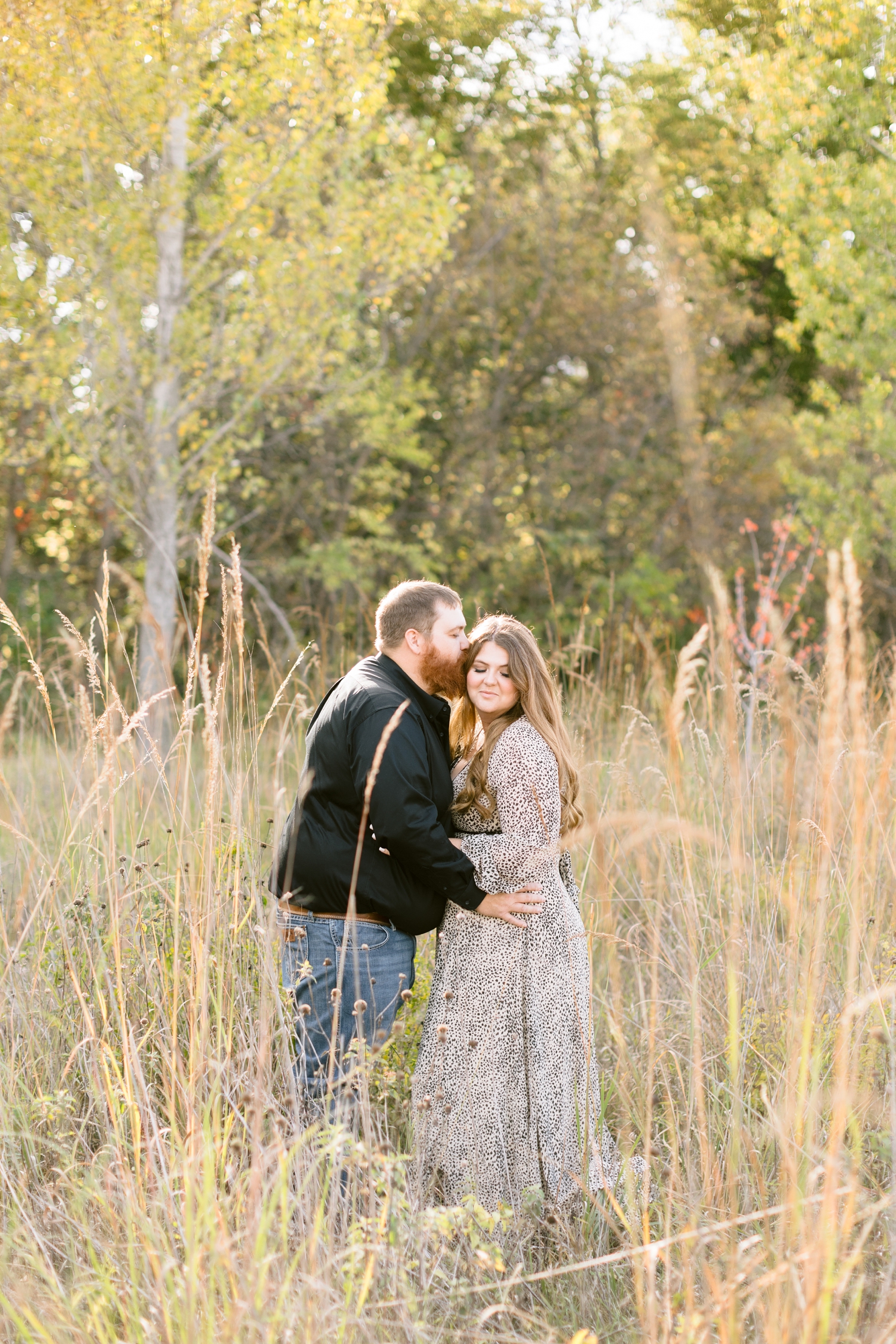 Trent kisses his bride-to-be on the cheek surrounded by fall foliage in a grassy field at Sheldon Park in Humboldt, IA | CB Studio