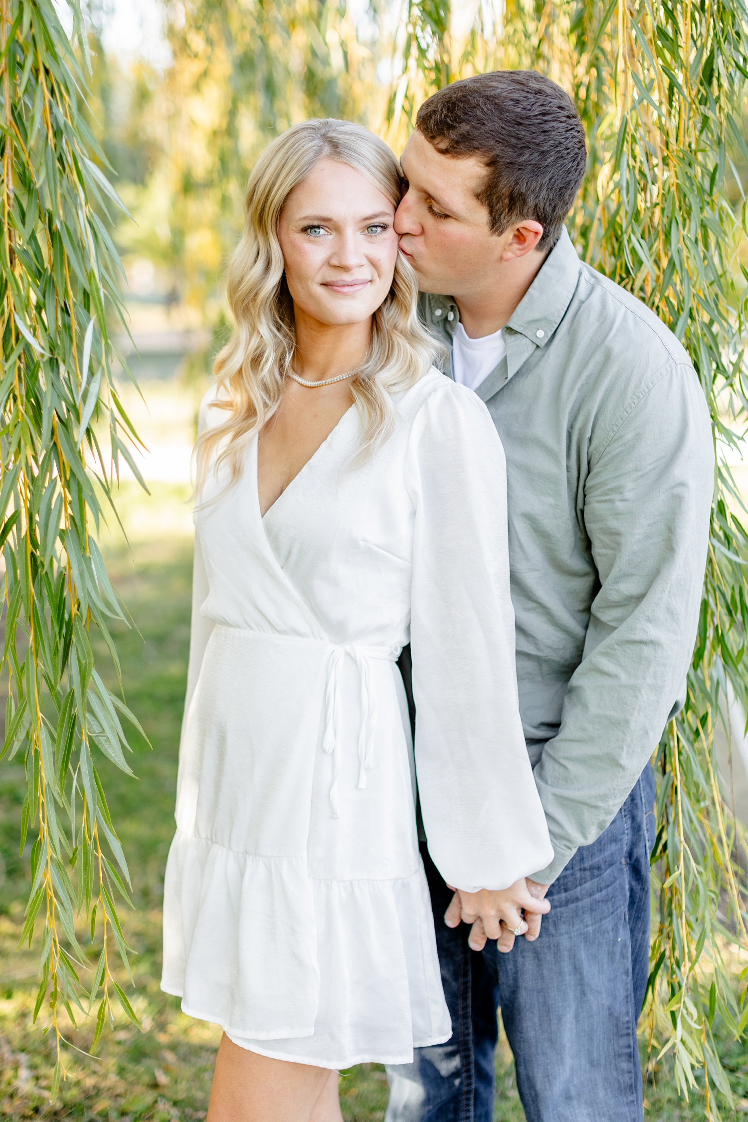 Reed kisses Nicole cheek underneath a large weeping willow tree at River Vally Orchards & Winery | CB Studio