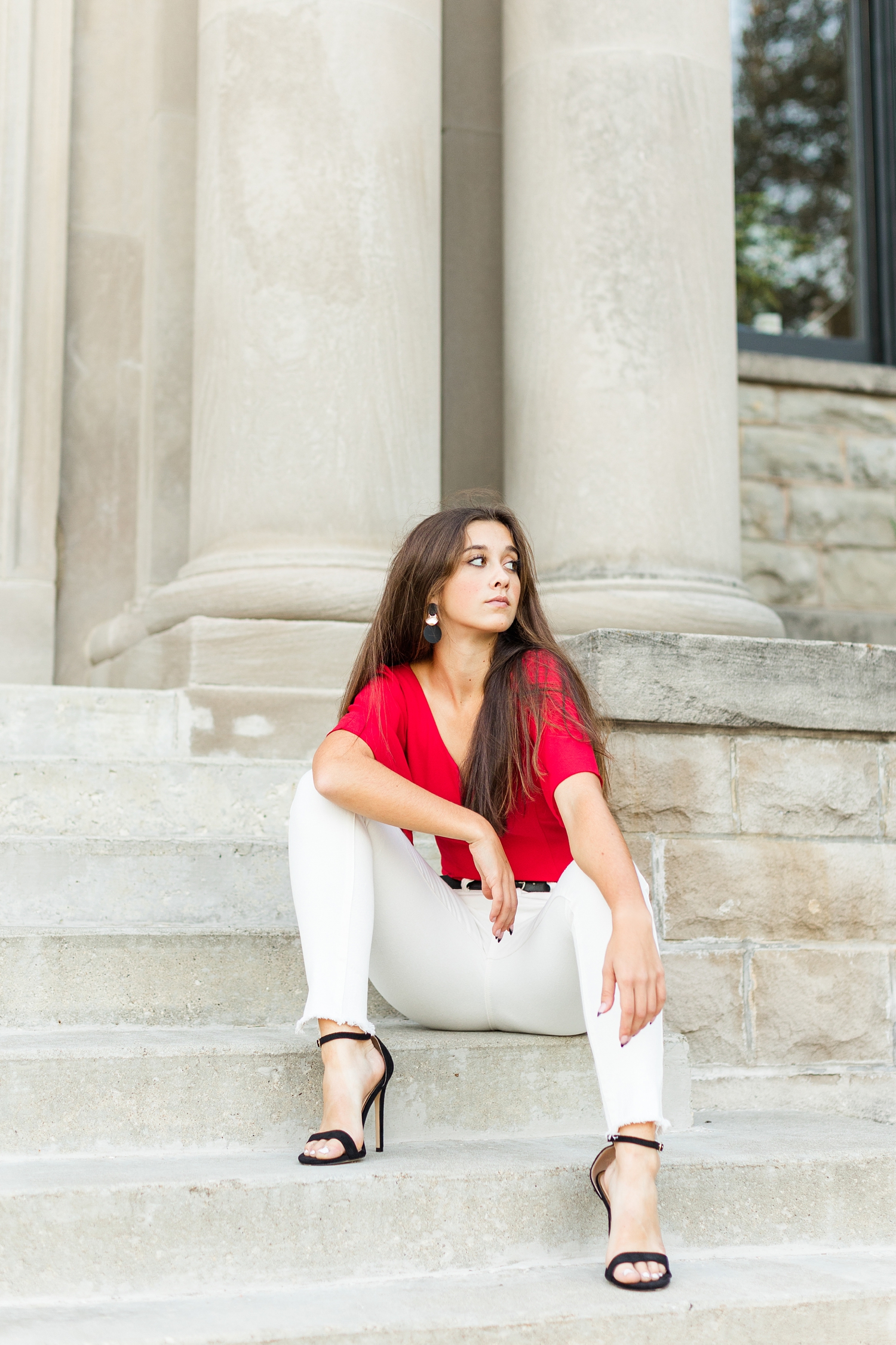 Sarah sits on concrete stairs and leans forward on her knees and she look off in the distance in front of the Humboldt Public Library | CB Studio