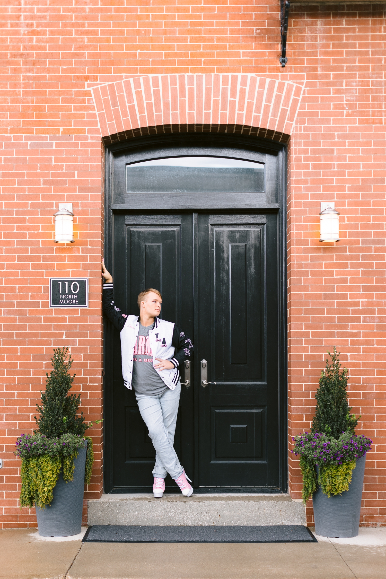 Seth leans against one side of a black doorway in downtown Algona wearing pink tennis shoe style high heels | CB Studio