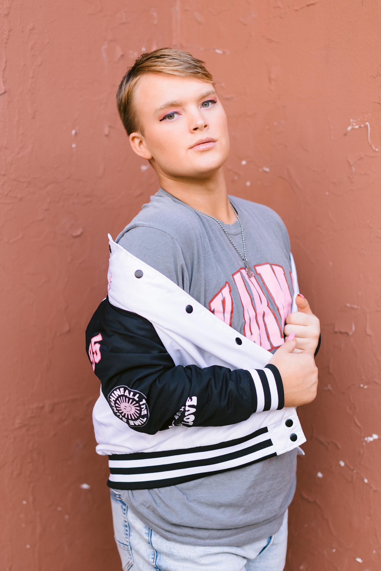 Seth pulls his jersey jacket over his shoulders as he stands in front of a pink wall in downtown Algona | CB Studio