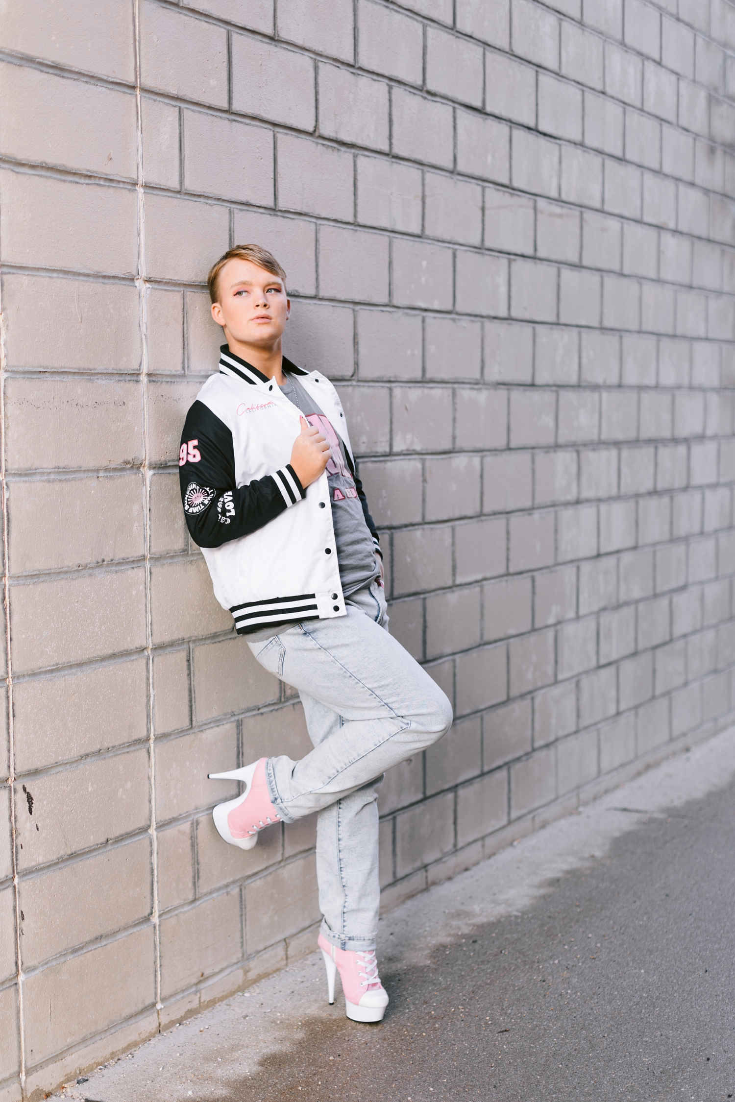 Seth leans against a neutral brick wall in downtown Algona wearing pink tennis shoe style high heels | CB Studio
