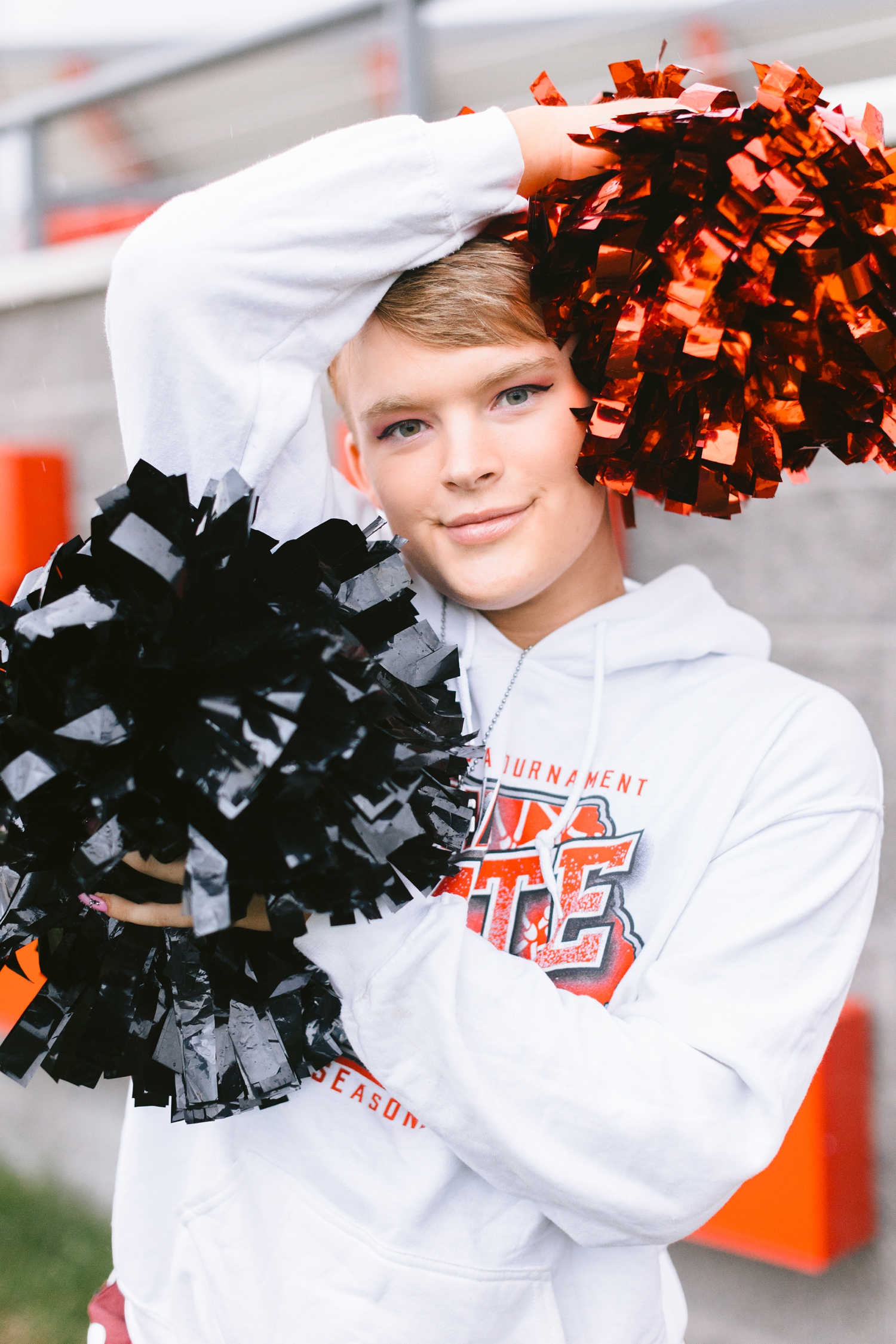 Seth smiles with his cheer poms surrounding his face on the Algona football field | CB Studio