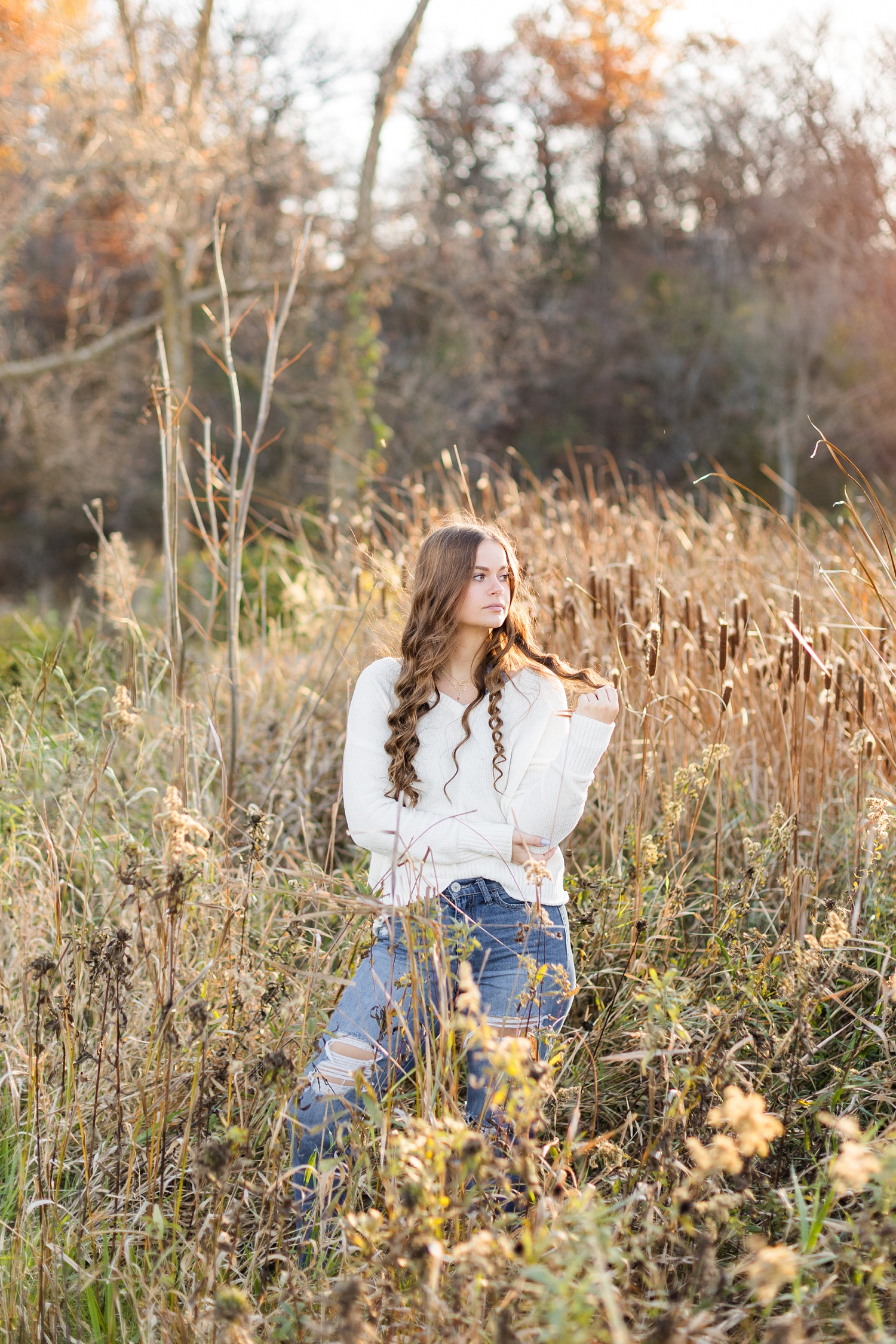 Avery stands in a grassy field filled with cattails at golden hour at Cottonwood Trail in Humboldt, IA | CB Studio