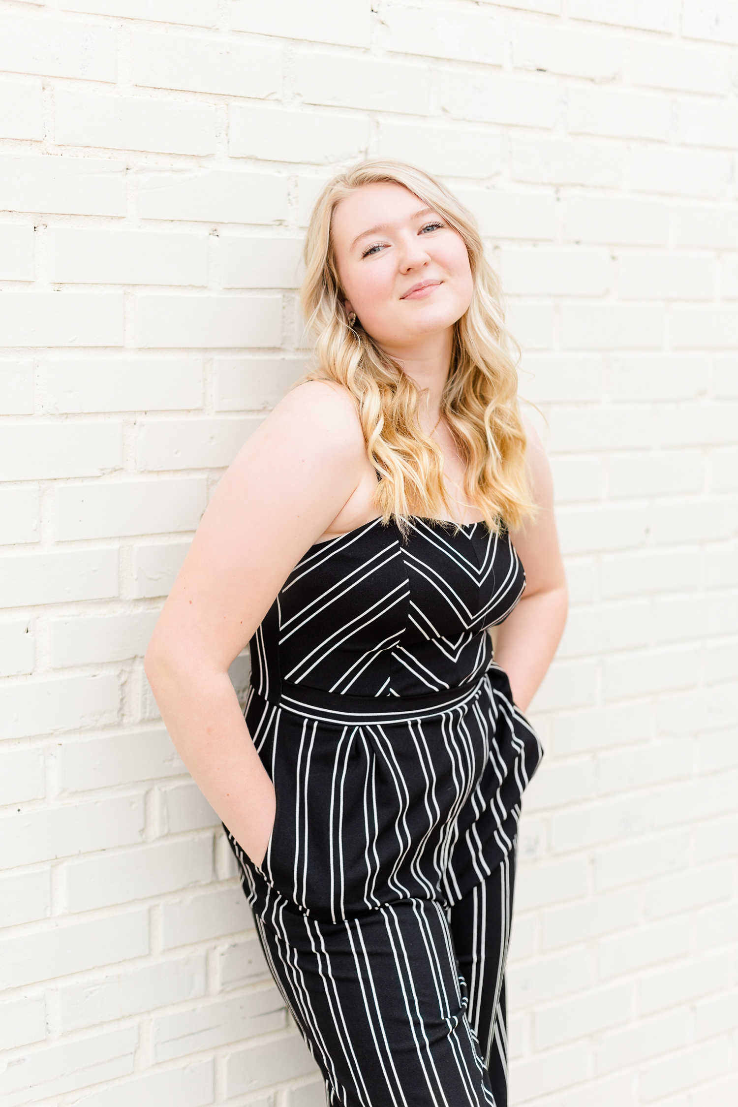 Jayden, wearing a black with white pinstripe, leans against a white brick wall in downtown Algona, IA | CB Studio