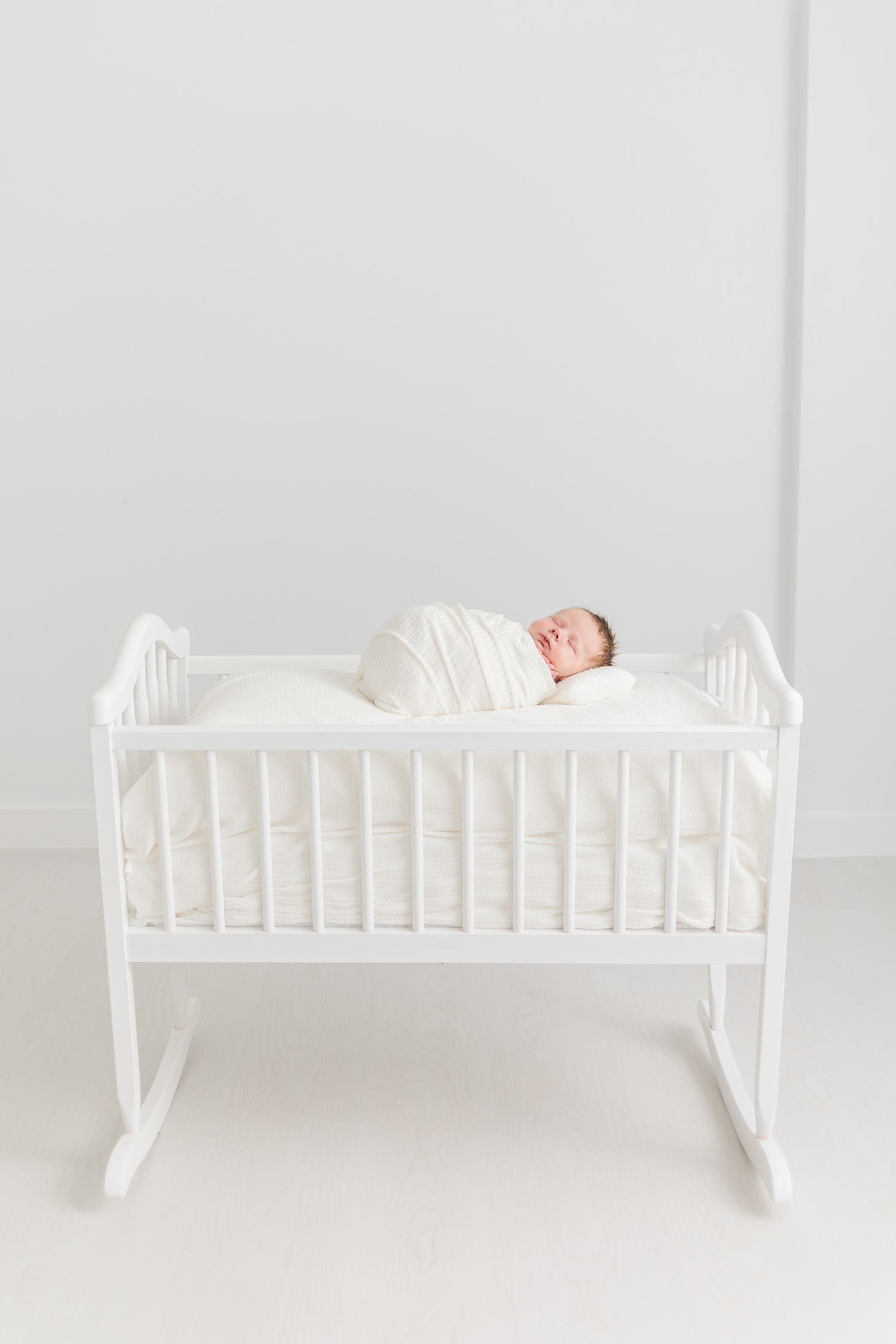 Baby Lane sleeps on an all wooden cradle in an all white room | CB Studio