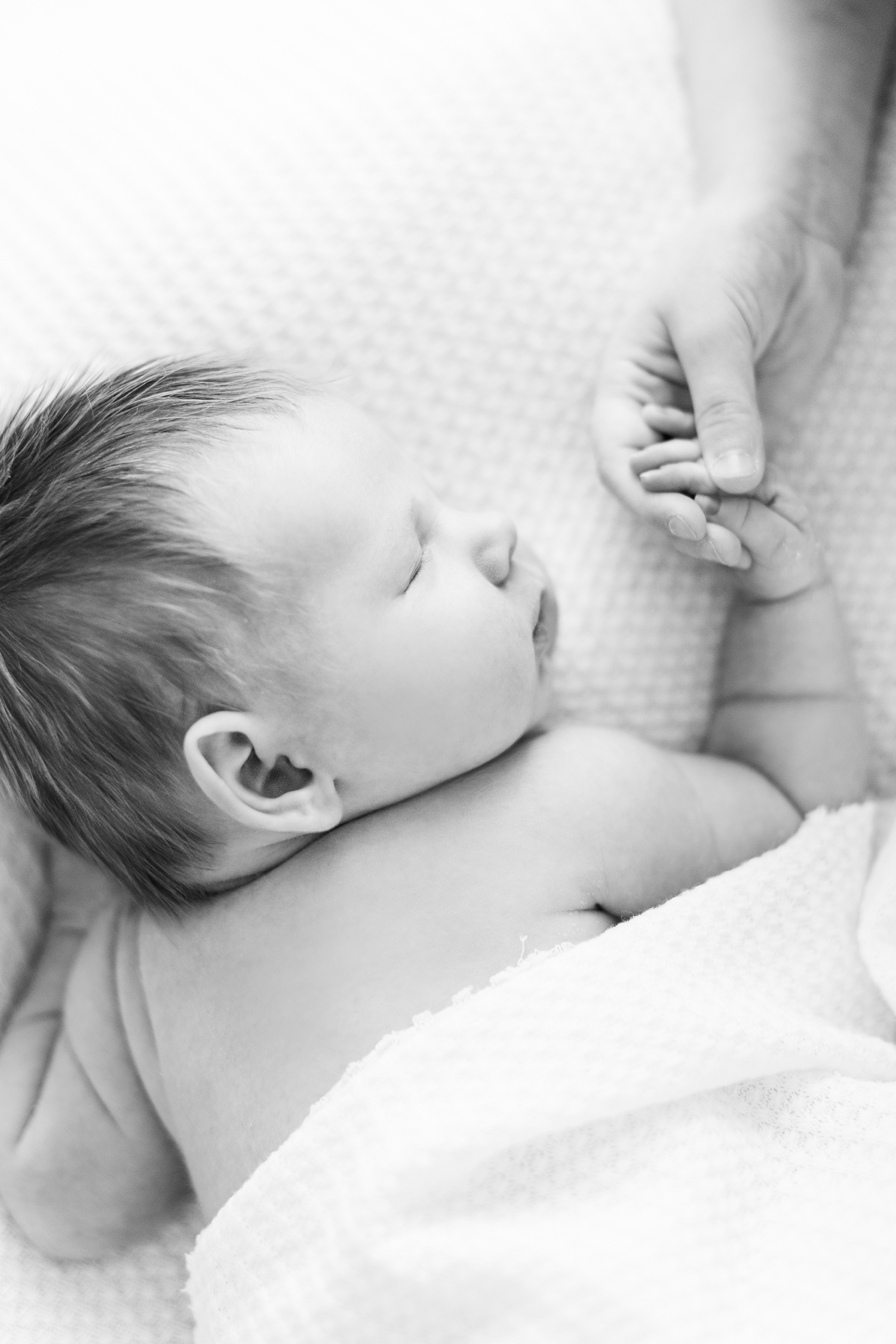 Baby Lane sleeps on an all white, waffle knit background while his big sister lightly holds his hand | CB Studio