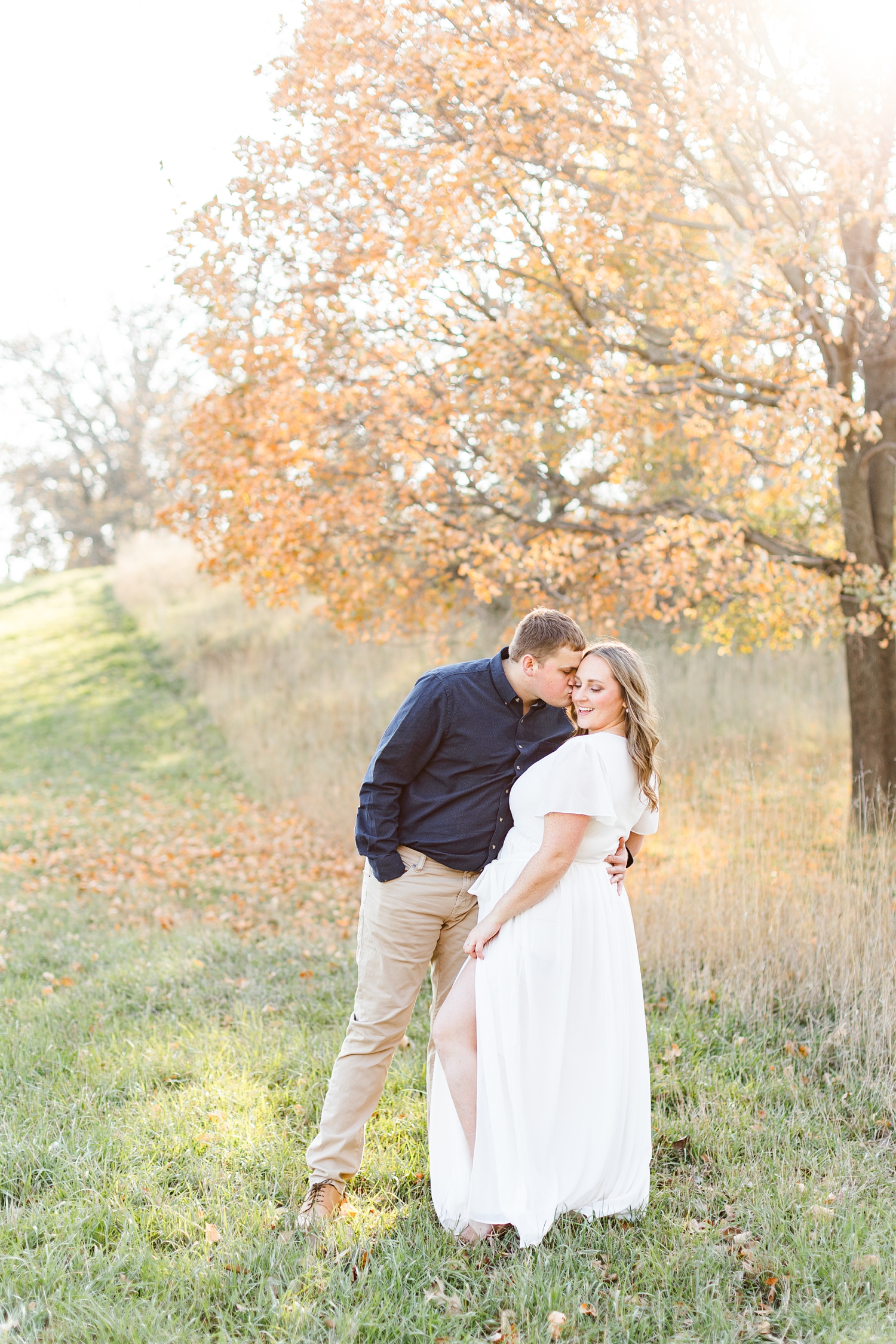Taylor dips Shelby back for a kiss on the cheek while standing in front of the perfect fall foliage tree in a grass pasture in Iowa | CB Studio