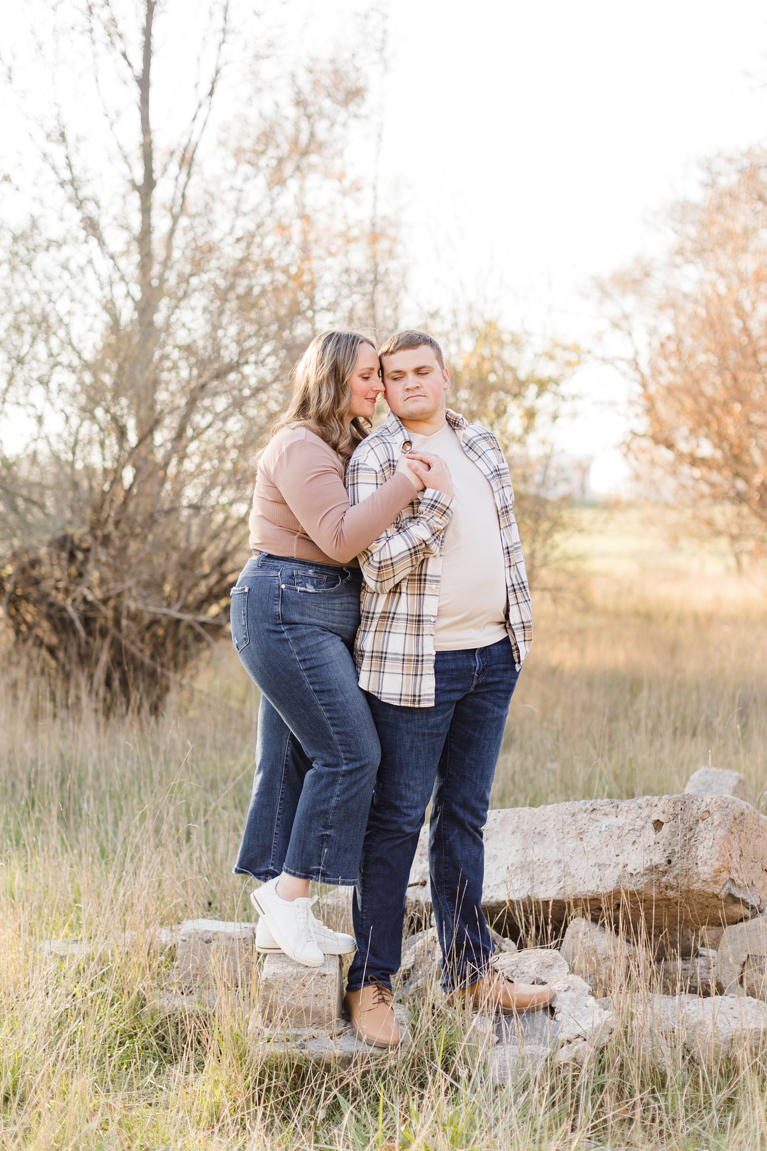 Taylor pulls Shelby's hand to his chest while Shelby nuzzles him as they both stand on a rock pile in a grass pasture in Iowa | CB Studio
