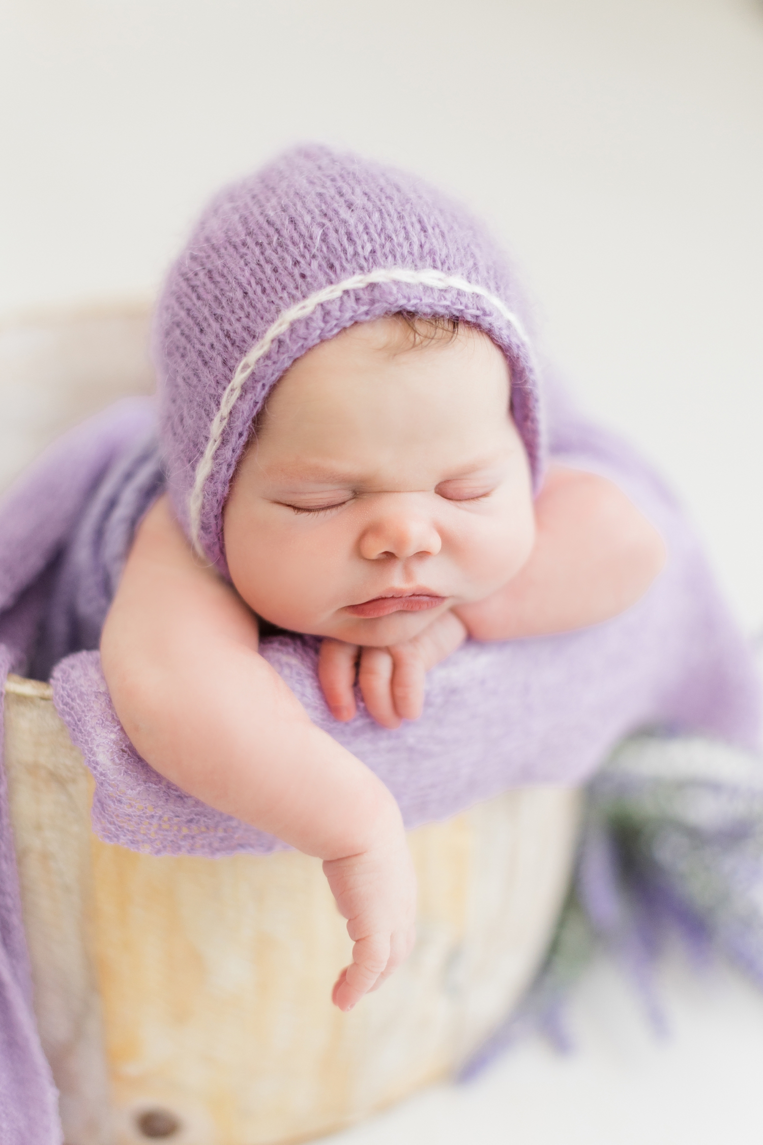 Baby Emersyn dressed in a purple bonnet sleeps peacefully in a bucket | CB Studio