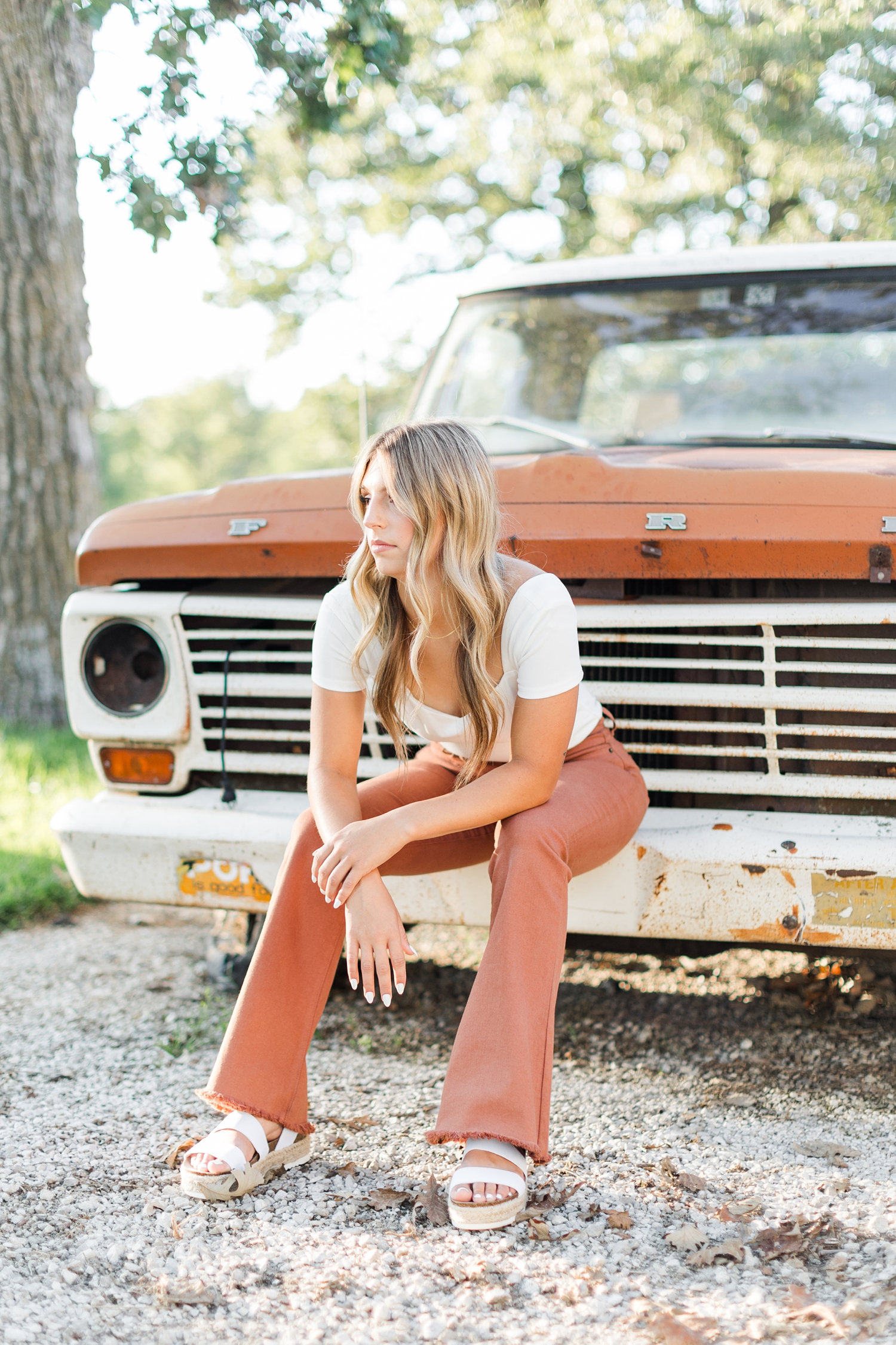 Eden, wearing a white top and burnt orange flared pants, sits on the bumper of a two-tone, white and burnt orange, 70's Ford truck | CB Studio