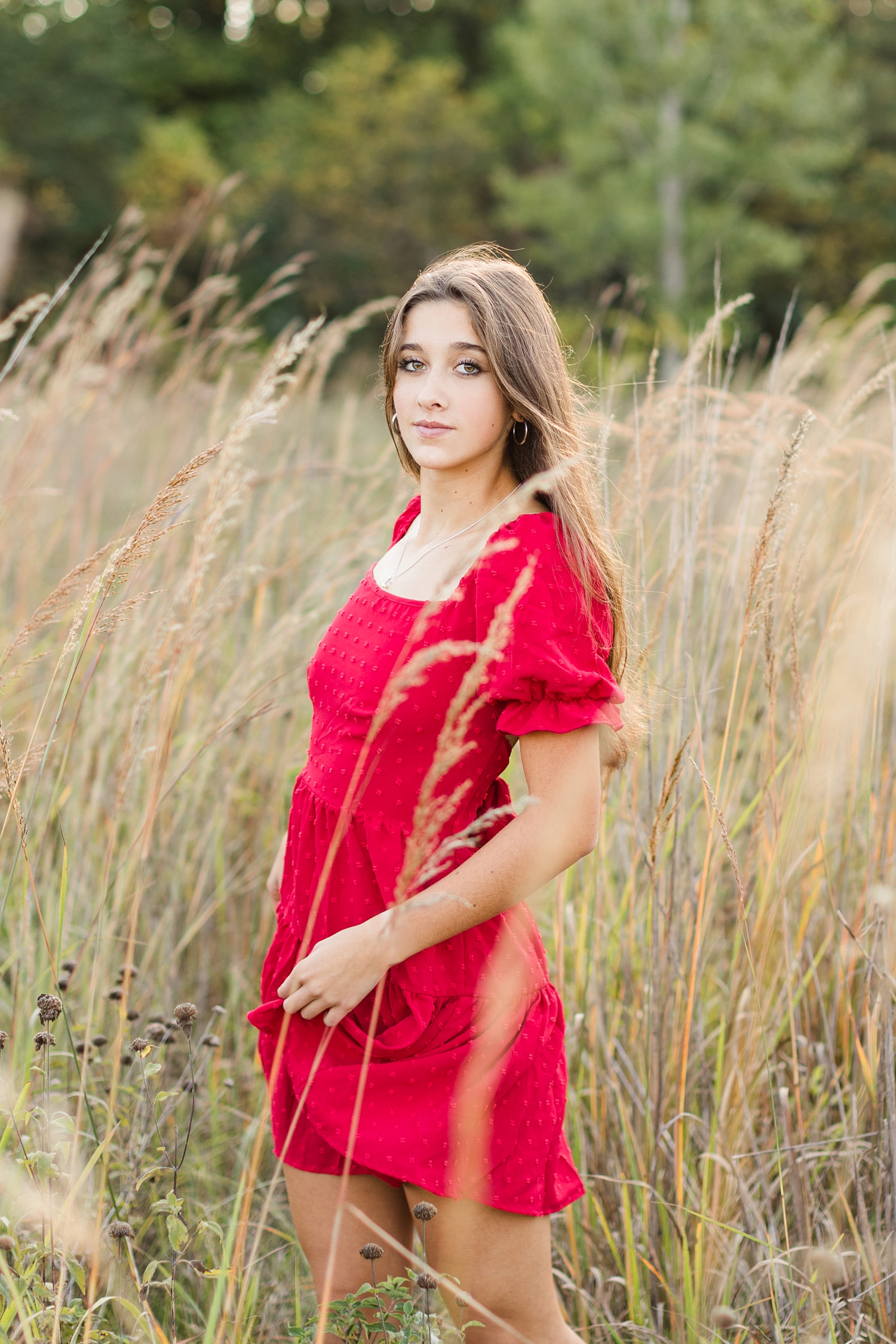 Sarah, wearing a red dress, walks in a grassy field in Iowa during the fall | CB Studio