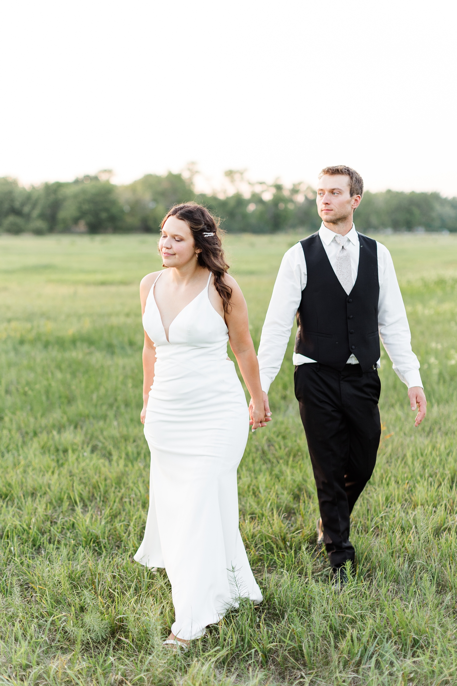 Alyssa takes her new groom's hand as they walk through a grassy field at sunset on their wedding day | CB Studio