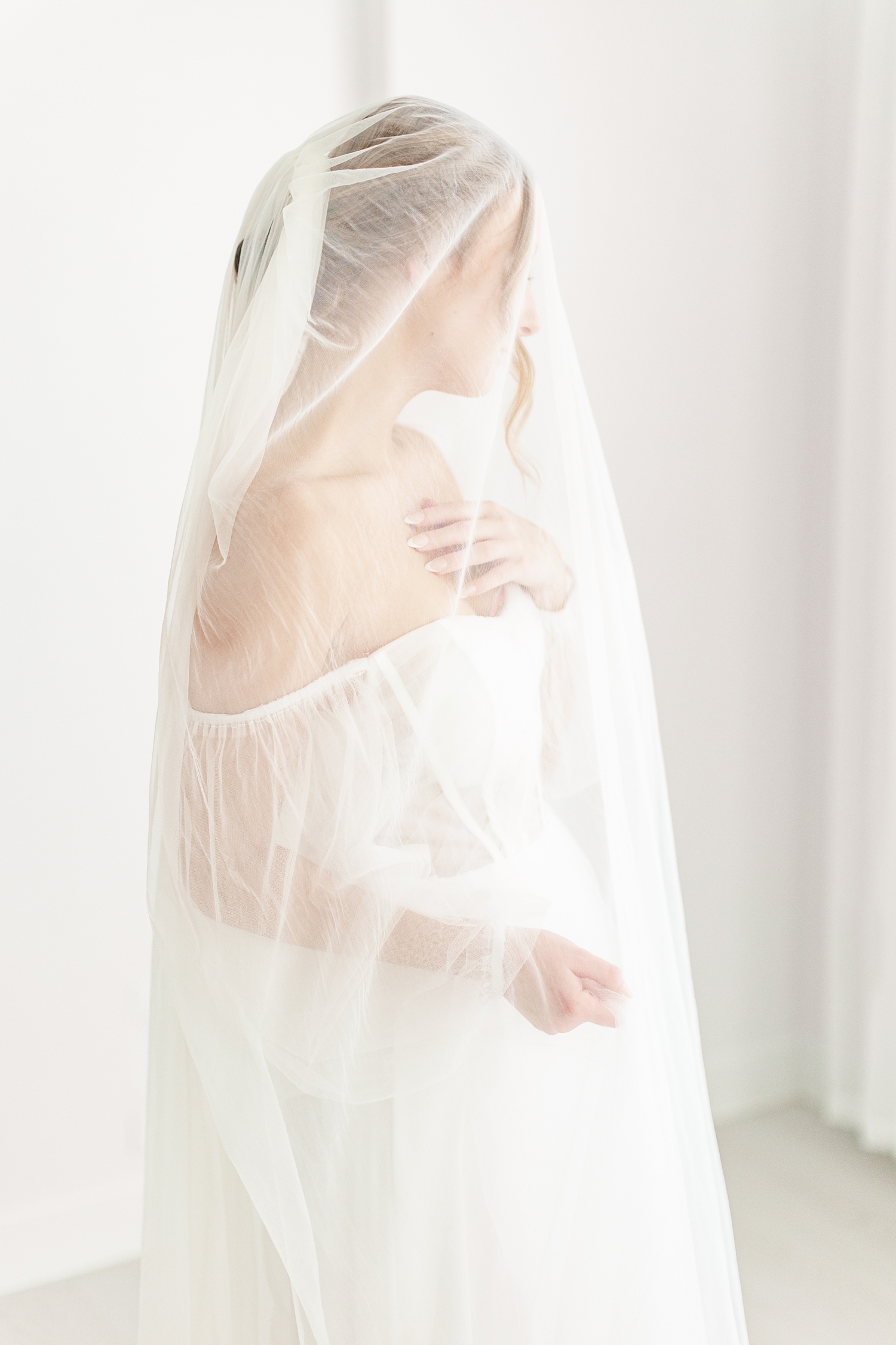 Bride, Ryley, draped in her cathedral length veil, holds part of her veil in one hand while the other graces her chest as she looks away | CB Studio
