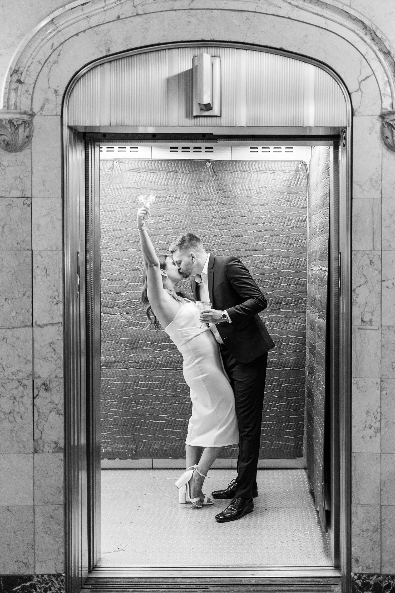 Jenna and Dustin kiss inside an elevator of The Equitable Building in Des Moines, IA while Jenna throws her champagne glass in the air | CB Studio