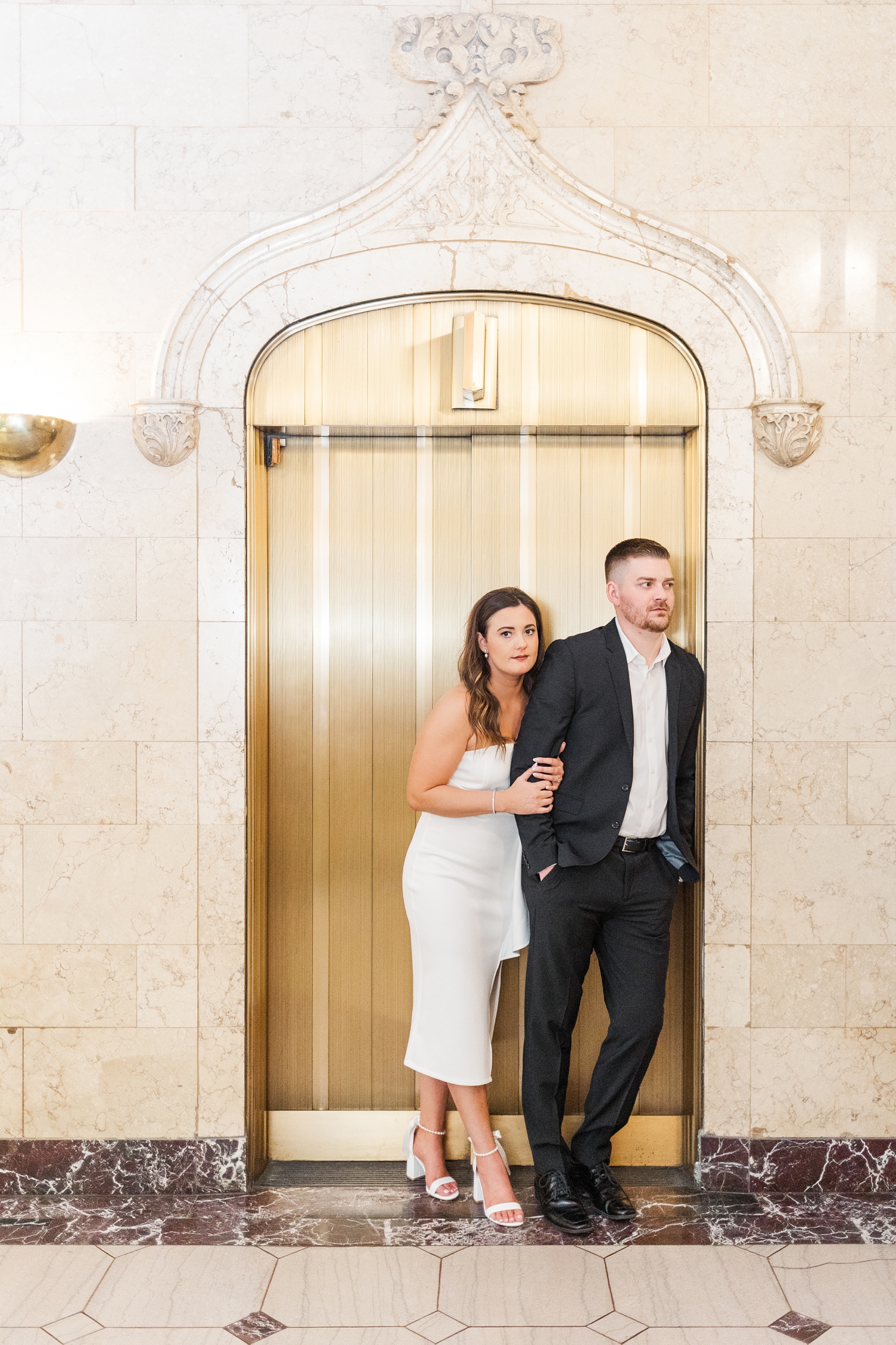 Jenna and Dustin lean against a gold elevator in the lobby entrance of The Equitable Building in Des Moines, IA | CB Studio
