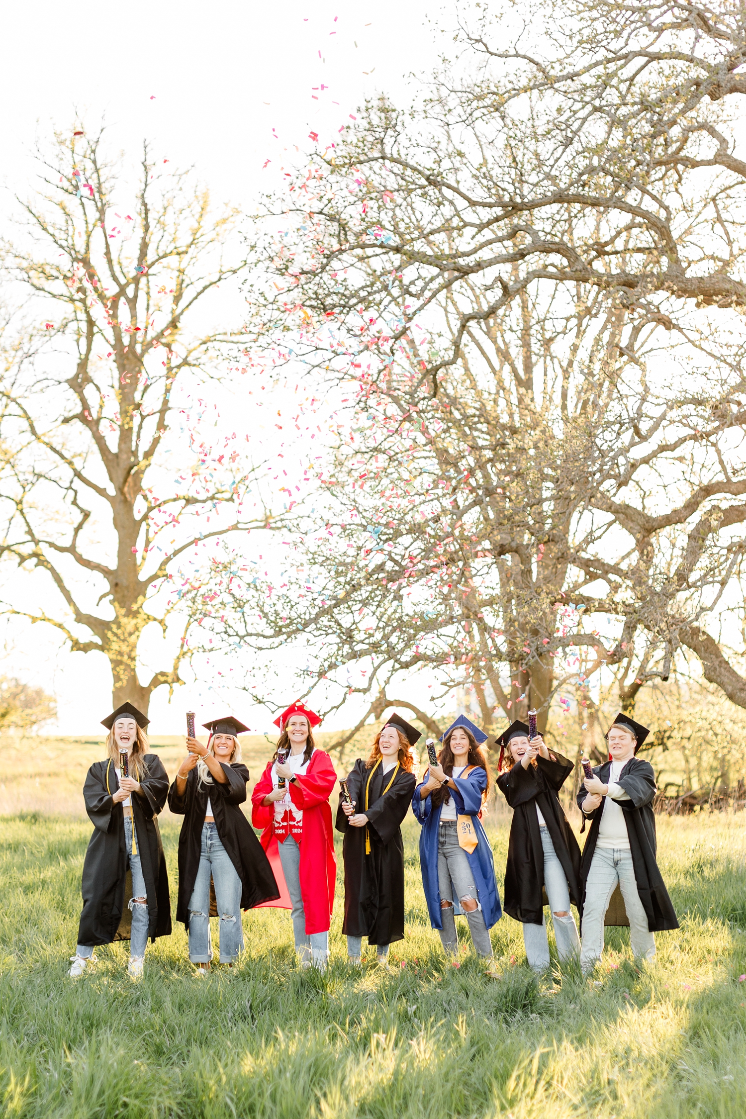 TEAM 24 shoot confetti canons in a grassy pasture while wearing their graduation cap & gowns to celebrate graduating high school Class of 2024 | CB Studio