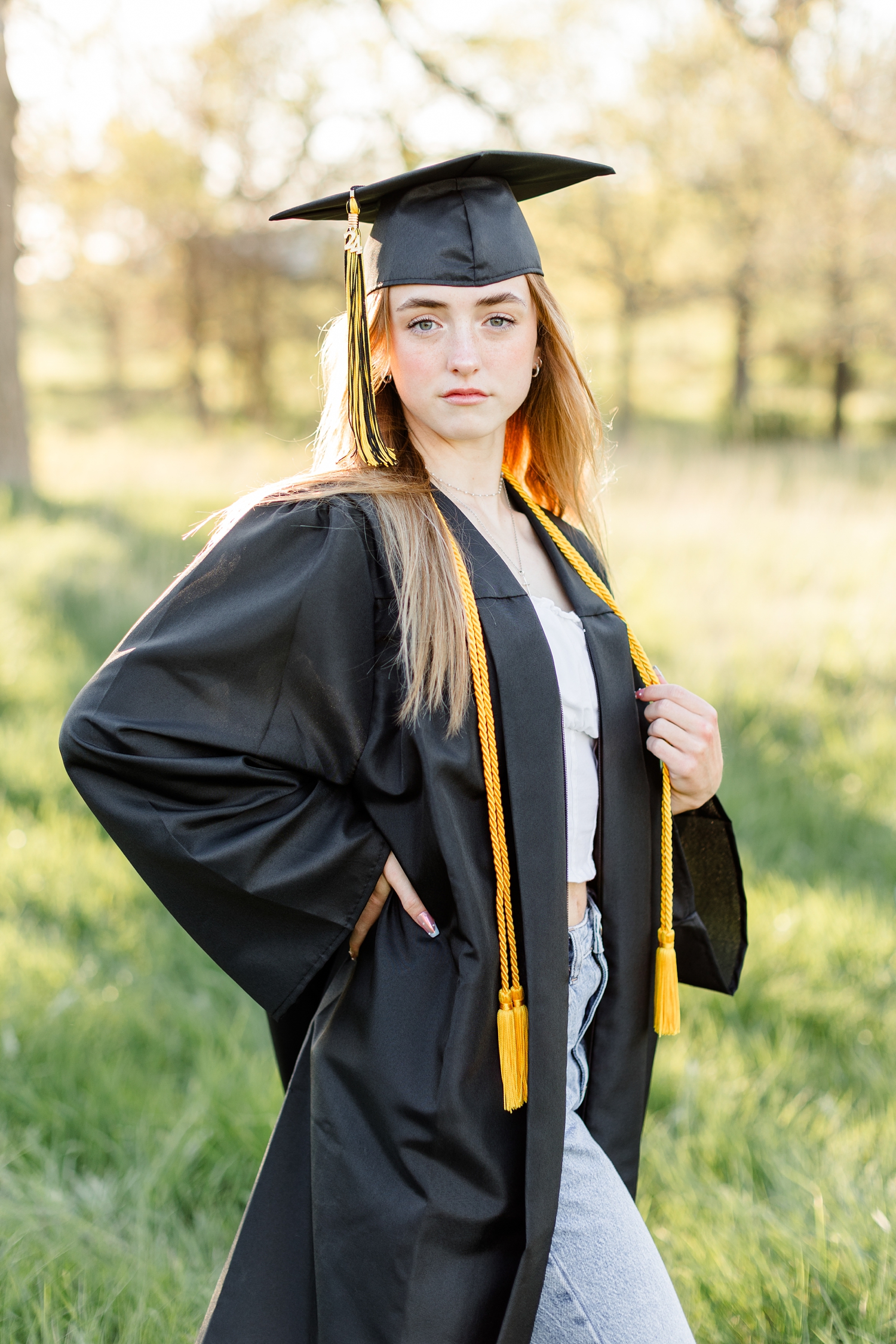 Reagan poses with her graduation cap and gown in a grassy pasture | CB Studio