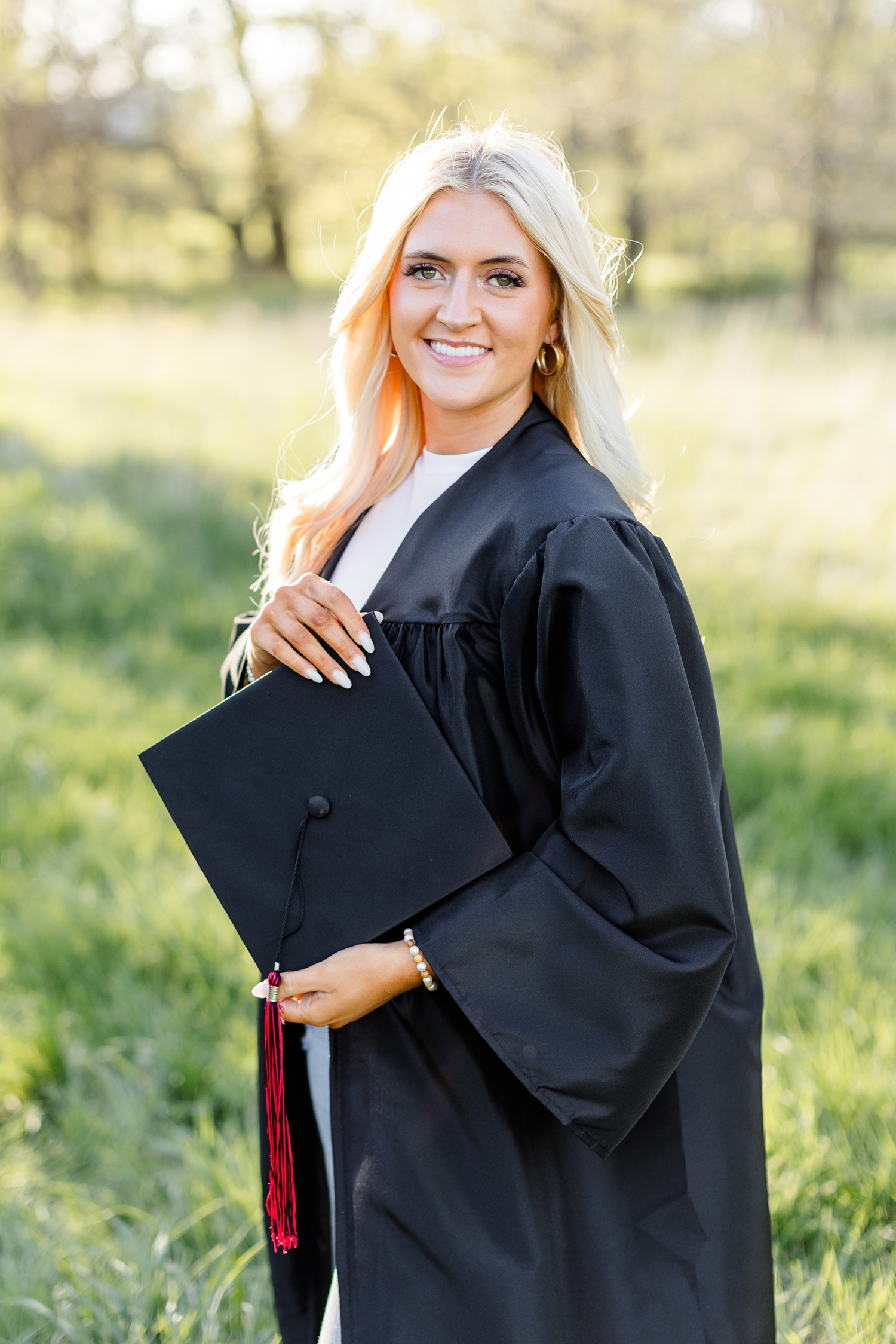 Jenna poses with her graduation cap and gown in a grassy pasture | CB Studio