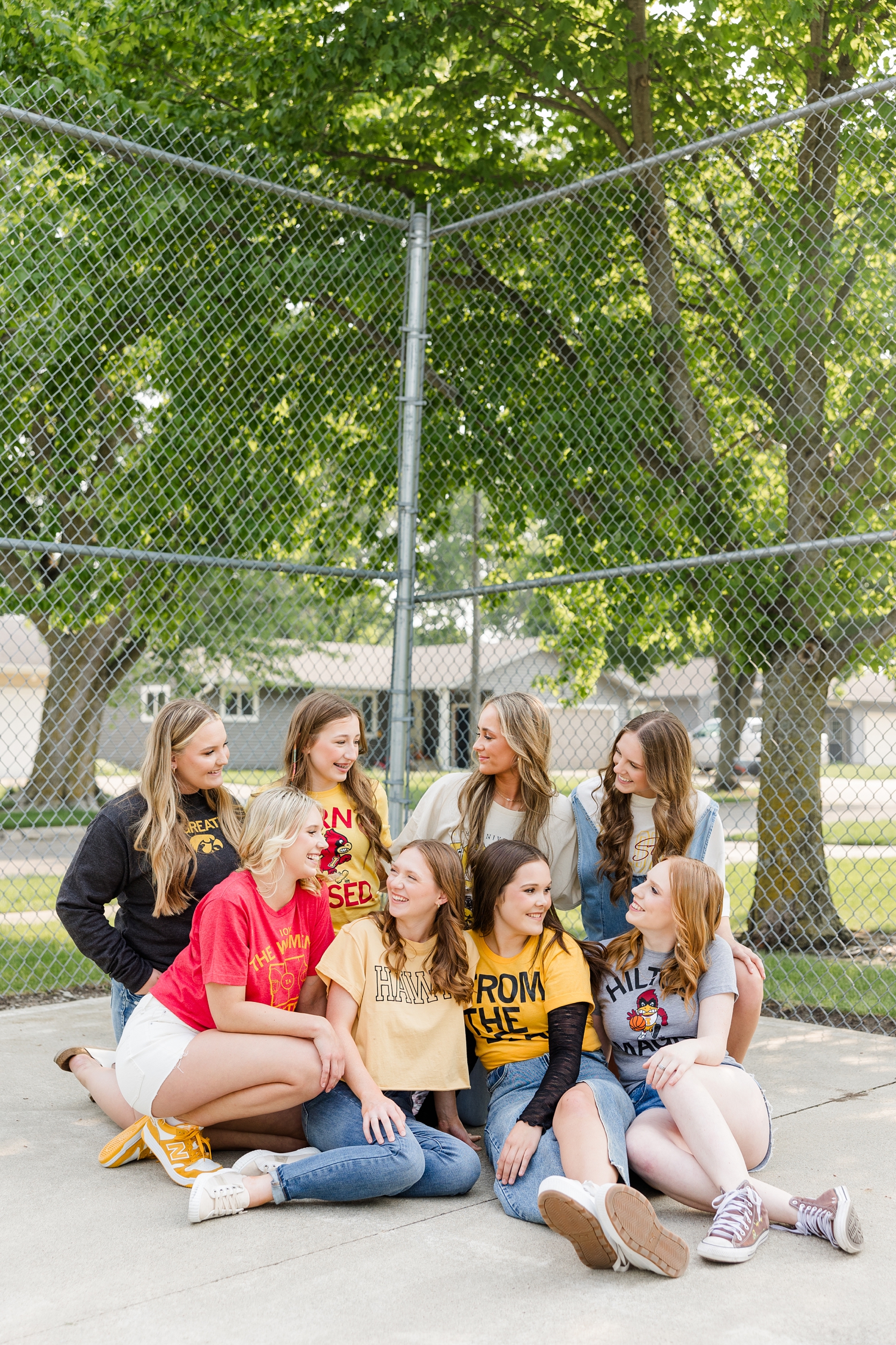 TEAM 25, all wearing Iowa or Iowa State clothing, sit in a group and smile at each other in an outdoor basketball court | CB Studio