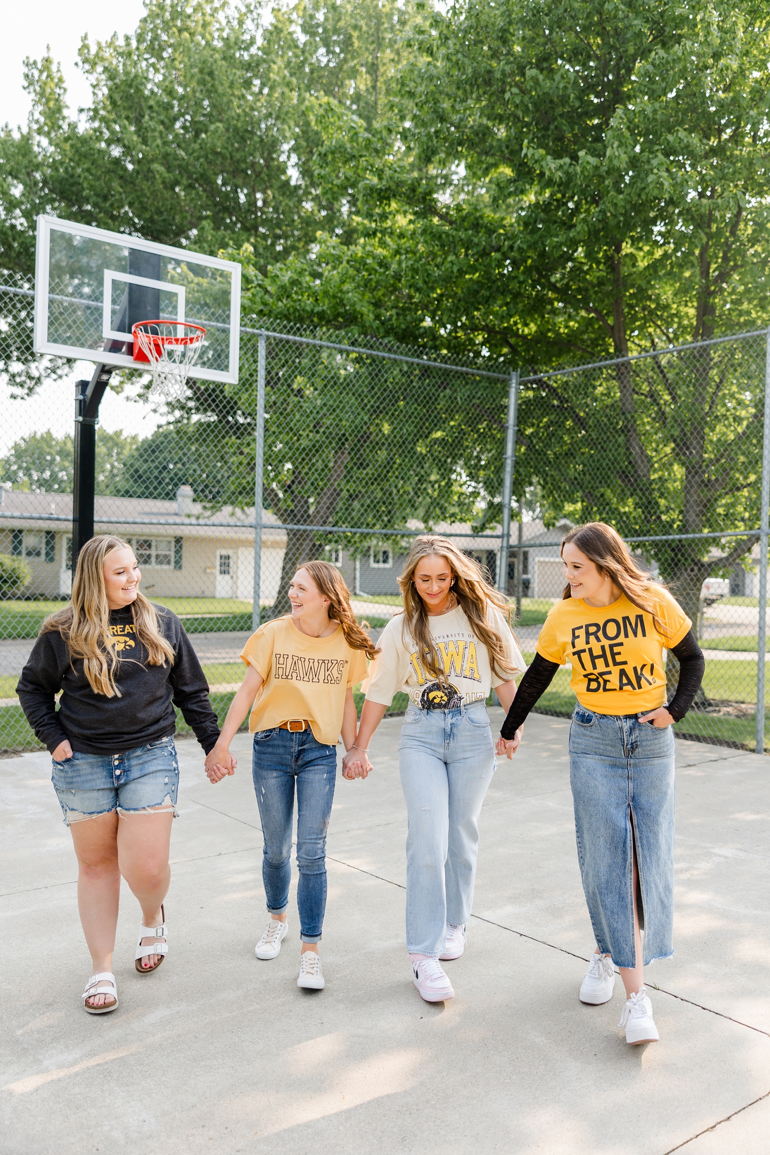 Four TEAM 25 girls, wearing Iowa clothing, walk hand in hand in an outdoor basketball court | CB Studio