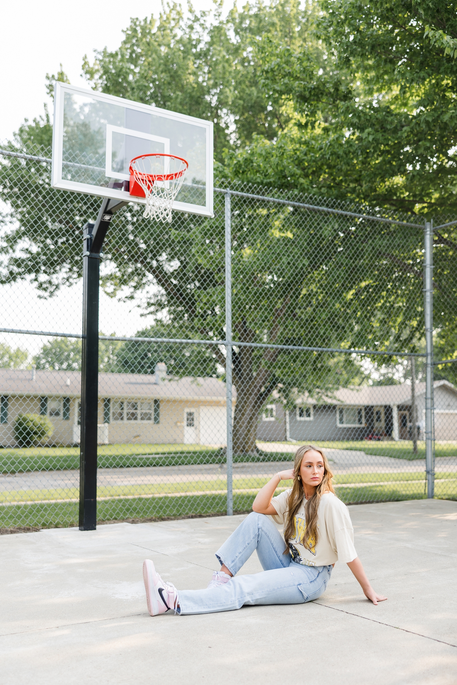 Blaire sits under an outdoor basketball hoop as she looks over her shoulder and off to the distance  | CB Studio