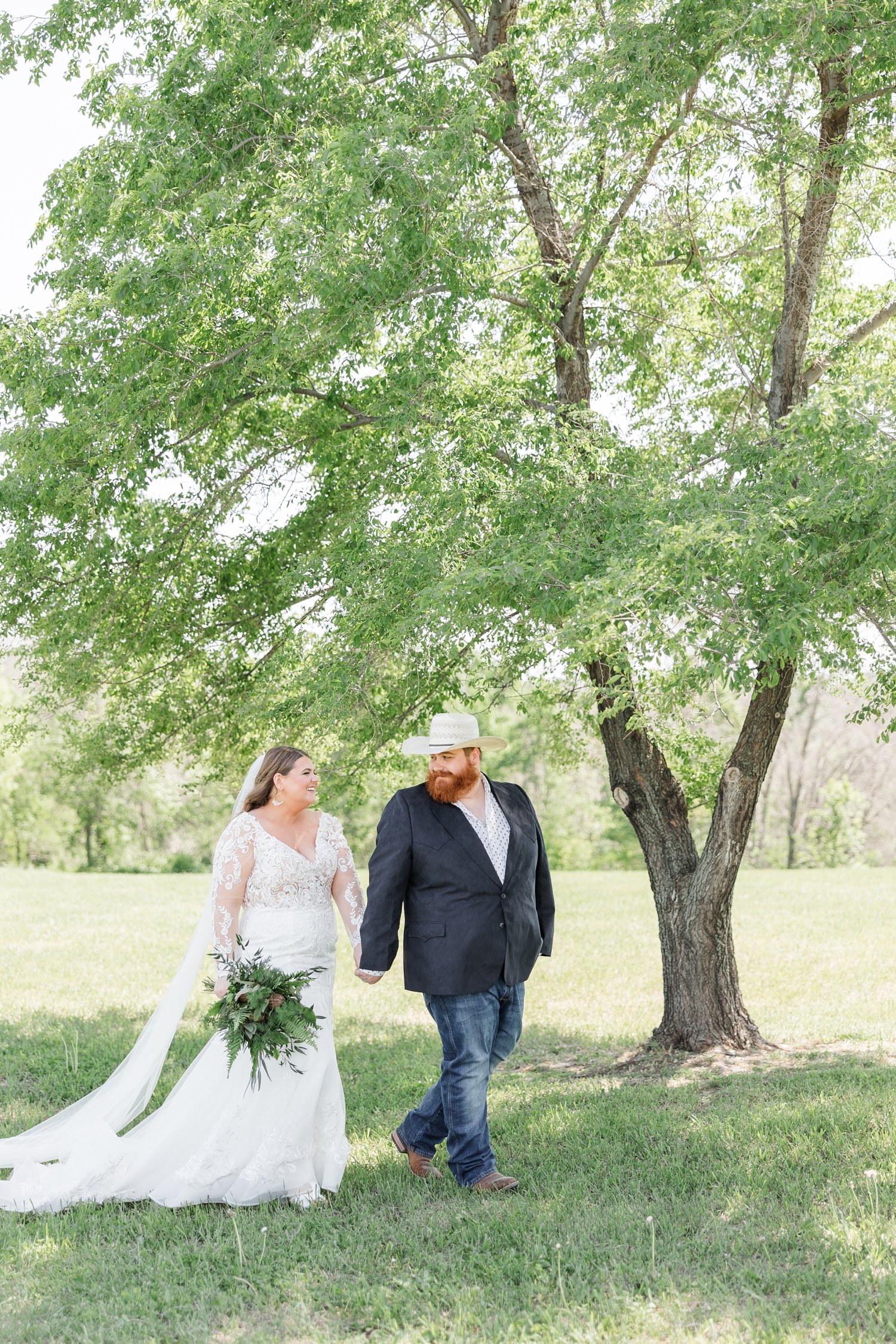 Trent leads his new bride, Neely, as they walk under a beautiful tree at Lizard Creek Ranch in Fort Dodge, IA | CB Studio