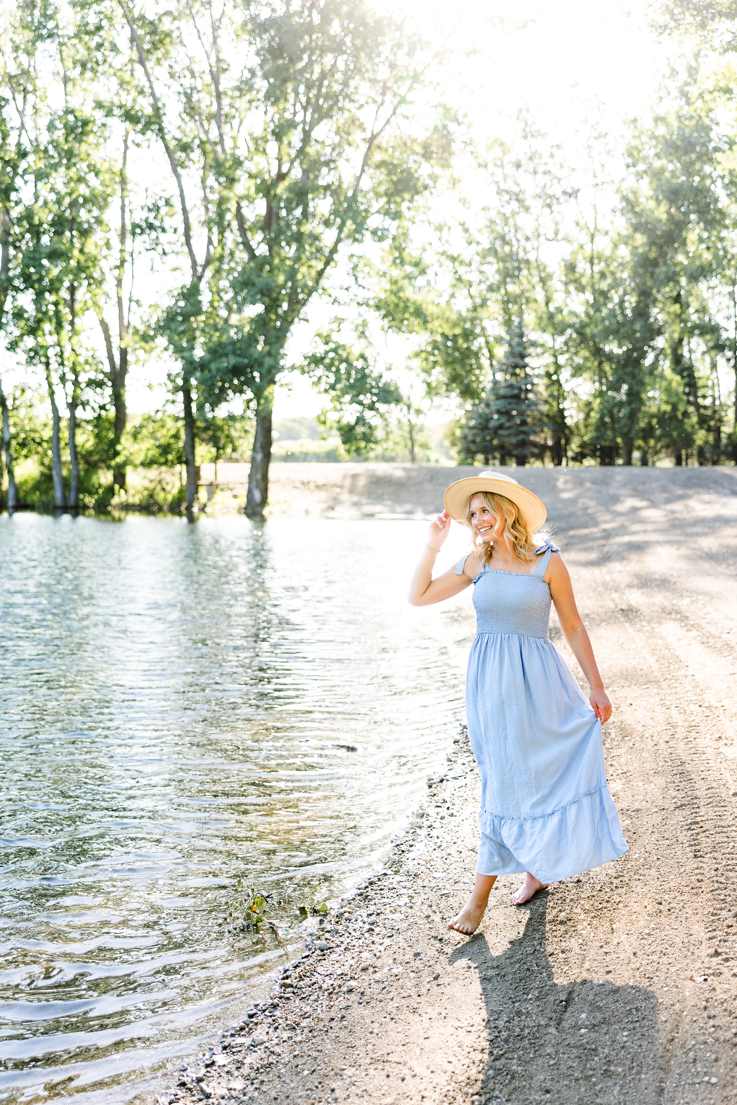 Addi, wearing a long blue dress and straw hat, walks along a pond at Wild Haven | CB Studio