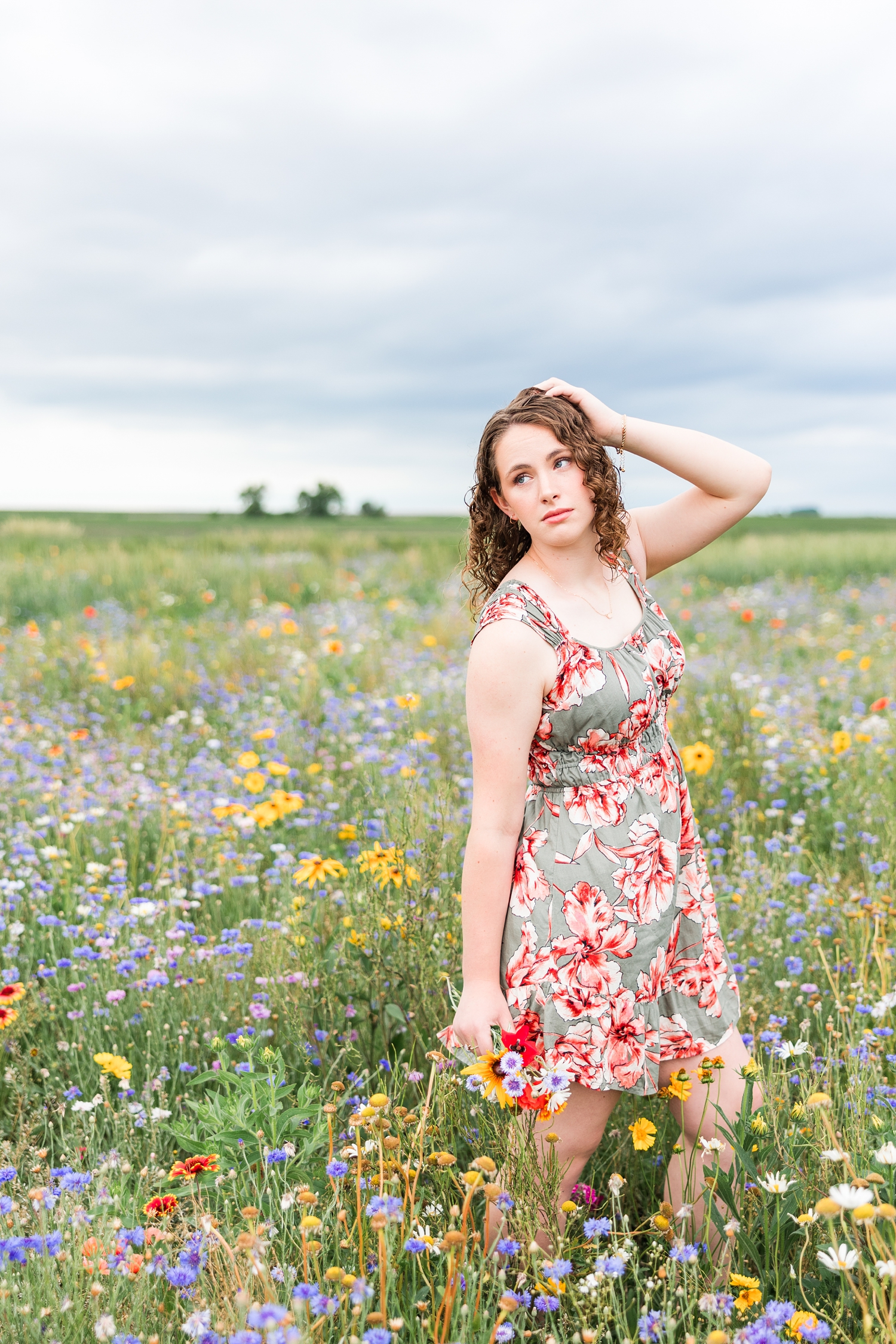 Alaina stands in a colorful wildflower field as she holds a flower bouquet in one hand and the other in her hair | CB Studio