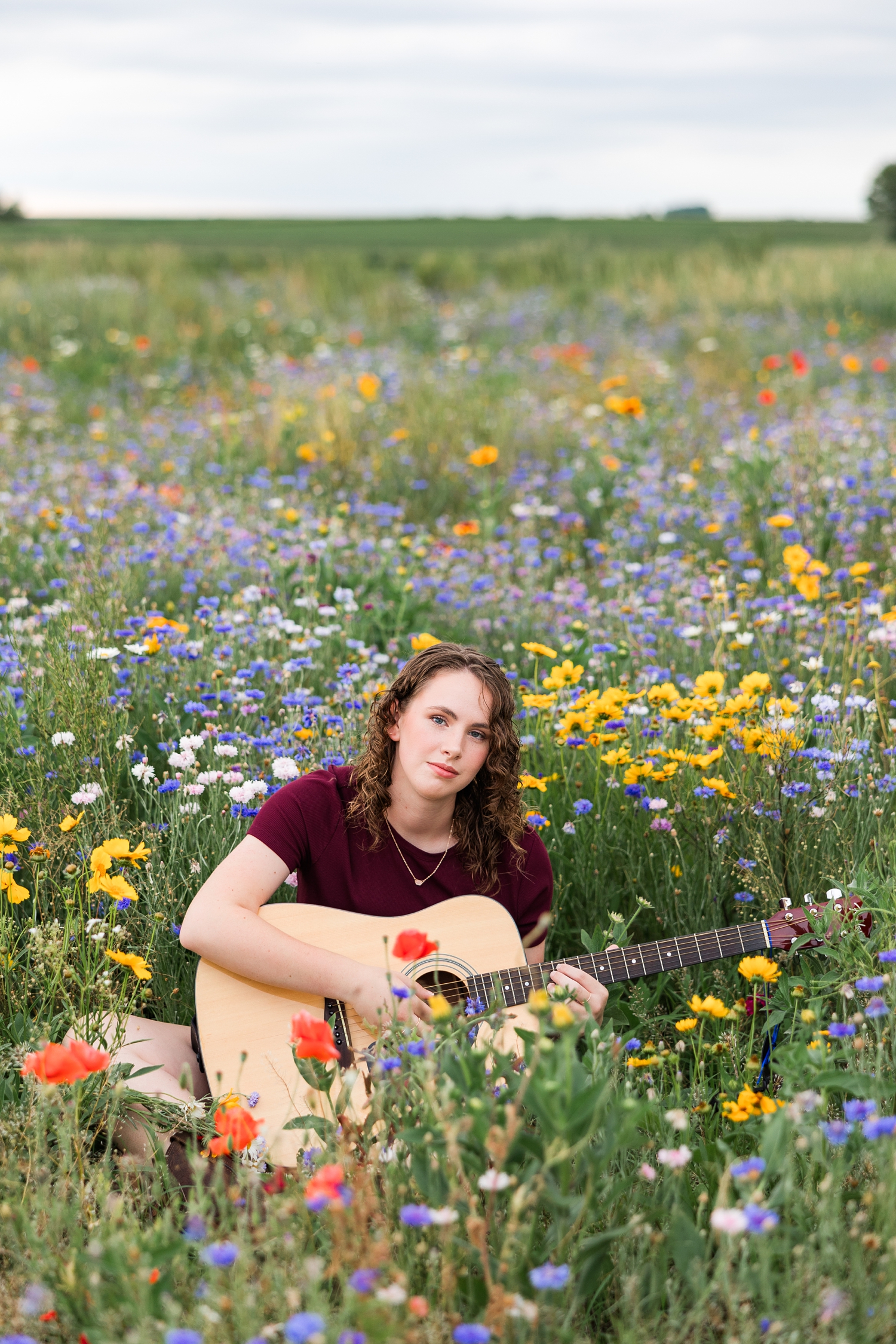 Alaina sits while she plays her guitar in a colorful wildflower field in Iowa | CB Studio