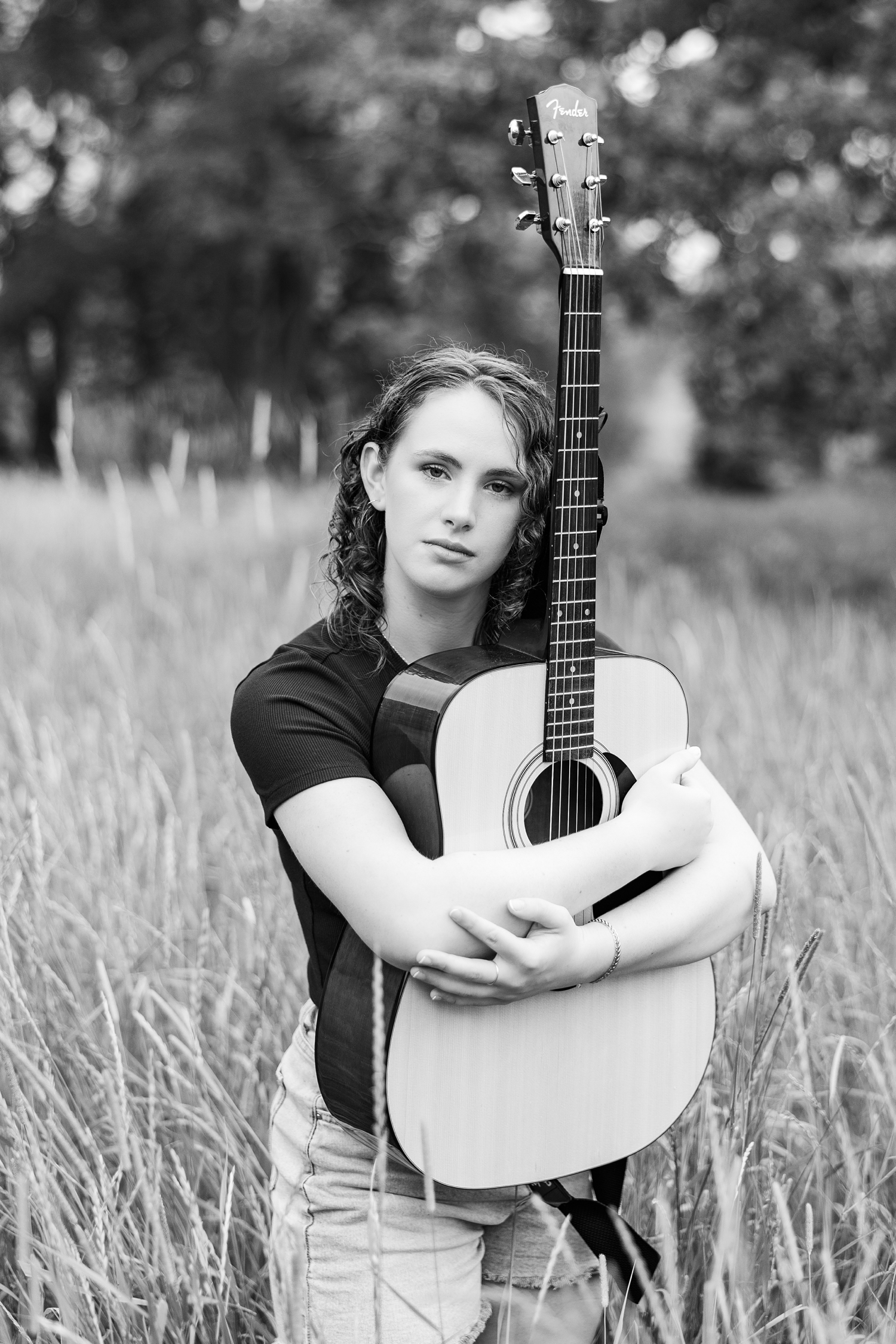 Alaina hugs her guitar as she stands in a grassy field in Iowa | CB Studio