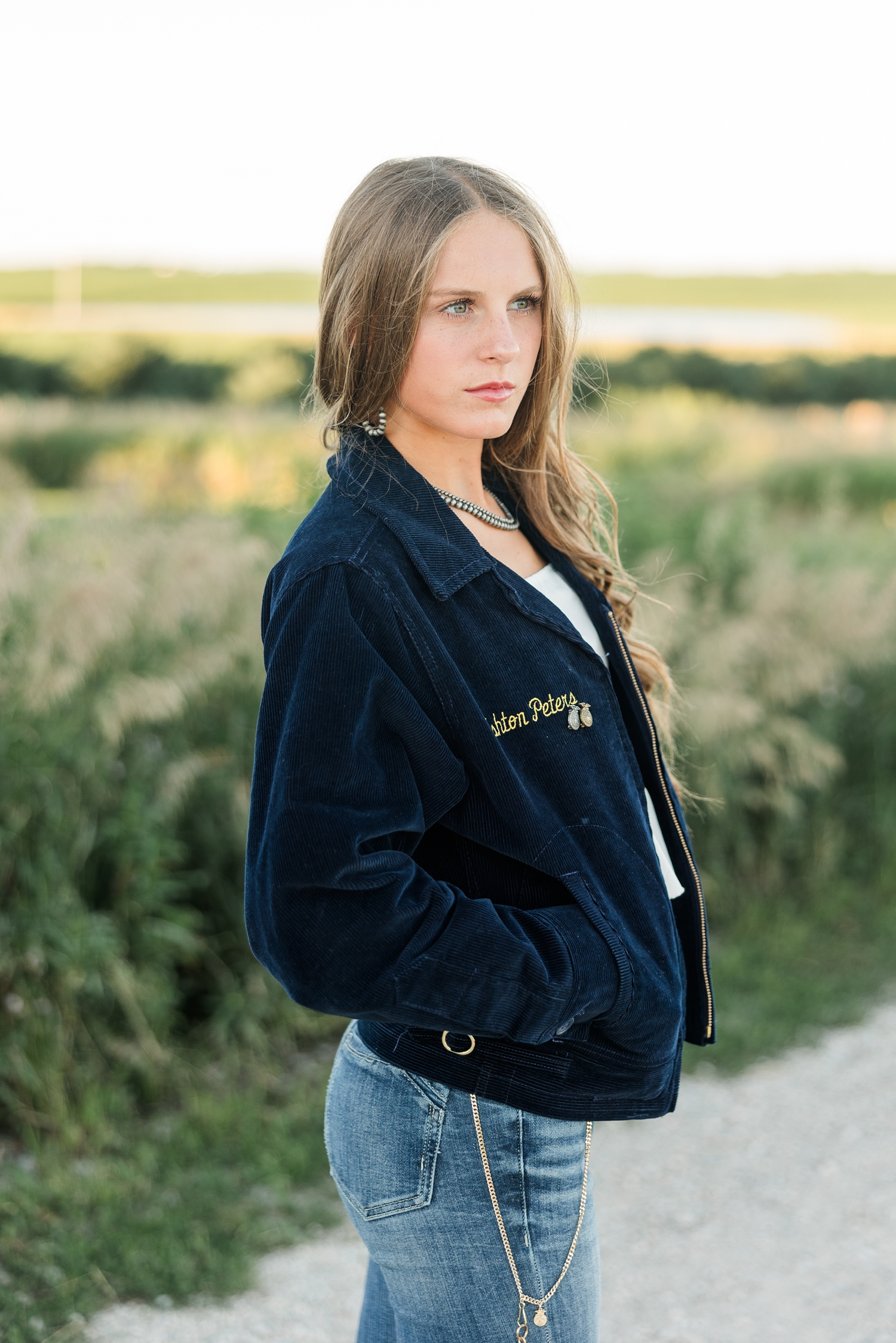 Ashton, wearing her FFA jacket, looks off in the distance as she stands on a gravel road | CB Studio