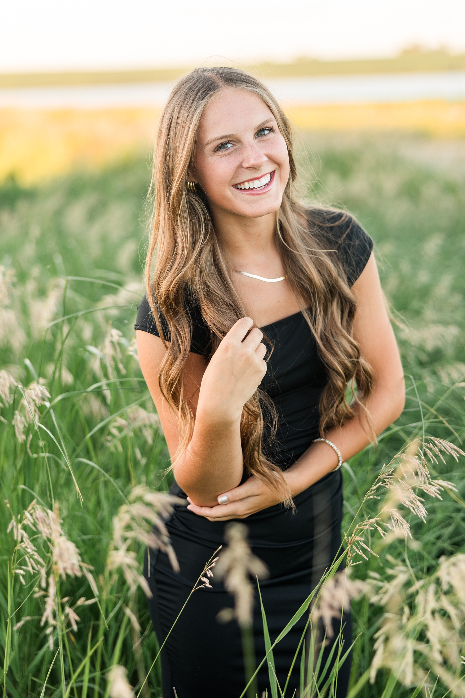 Ashton, wearing a black formal dress, laughs towards the camera as she stands in a grassy pasture | CB Studio