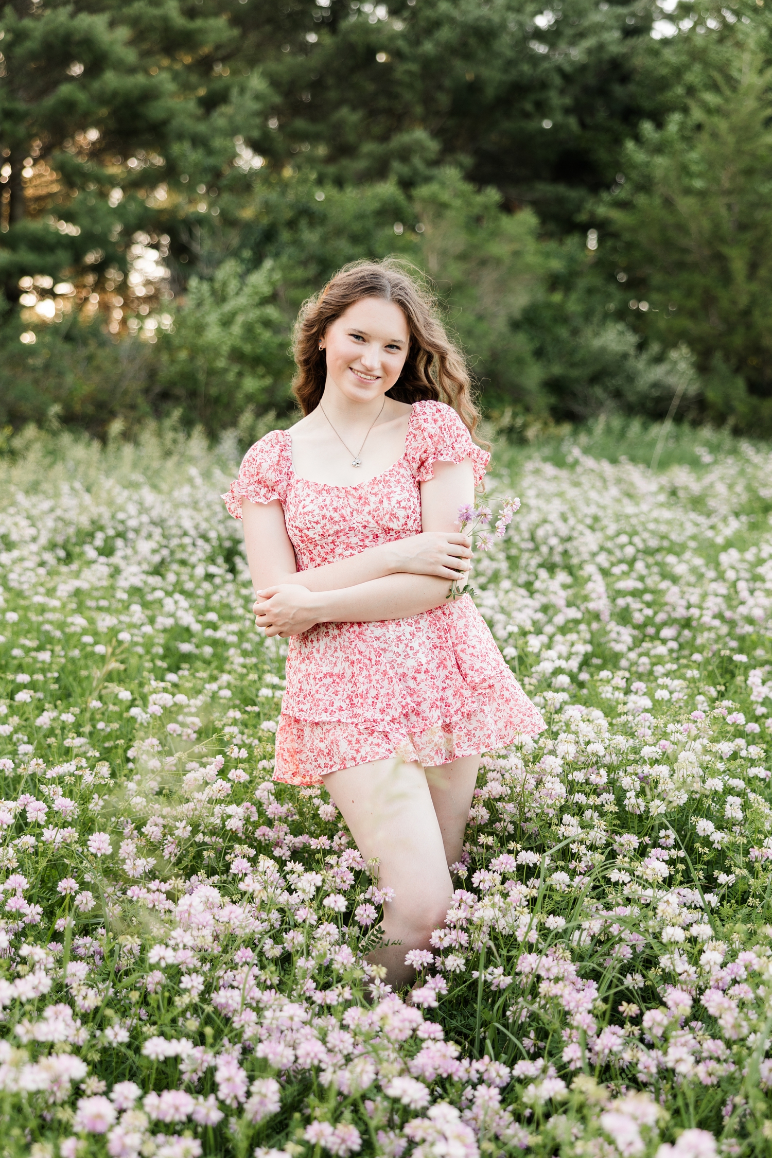 Evie, wearing a pink floral romper, stands in the middle of a flower field at Water's Edge Nature Center with her hands wrapped around her arms | CB Studio