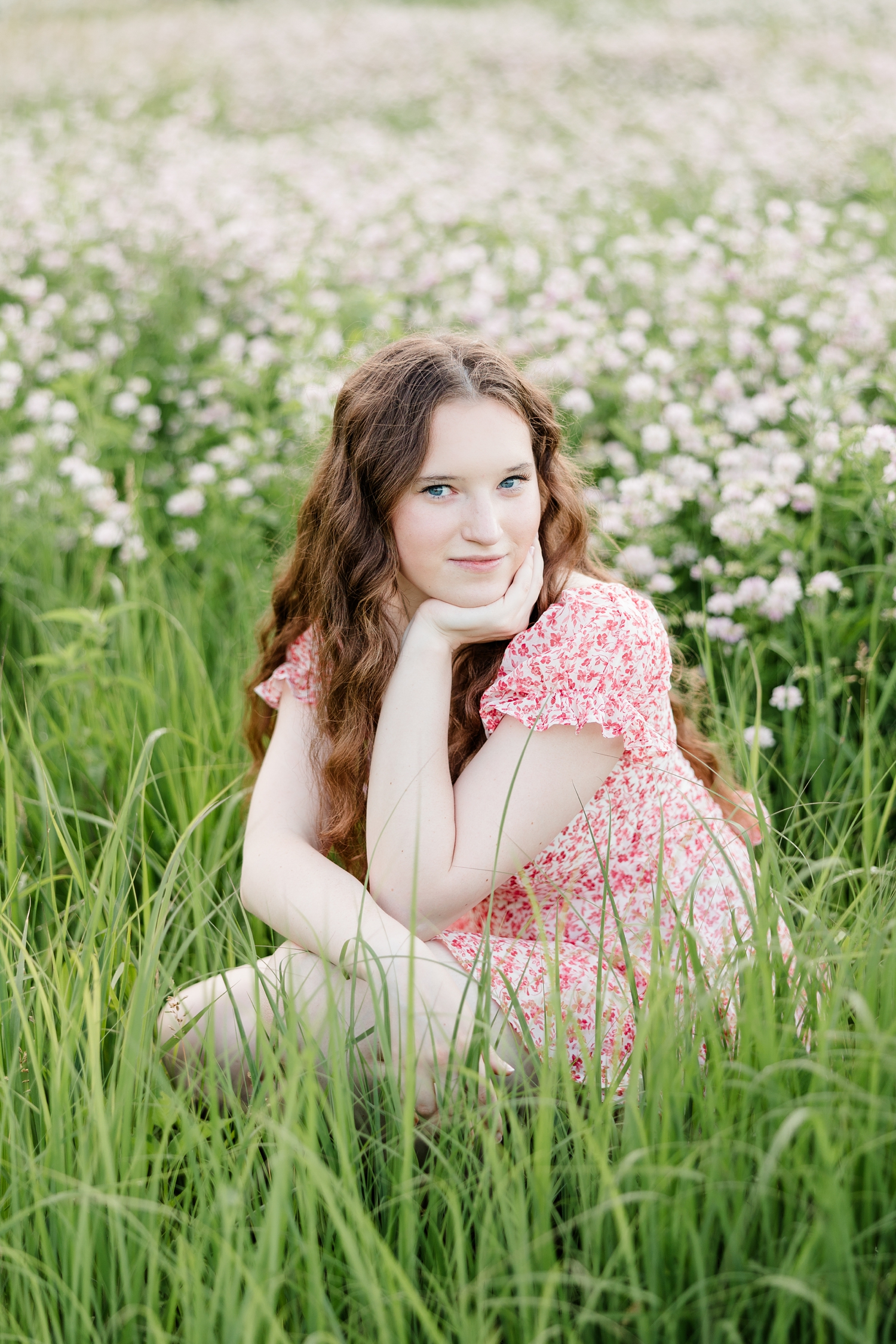 Evie, wearing a pink floral romper, sits in the middle of a flower field at Water's Edge Nature Center with her chin in her hand | CB Studio