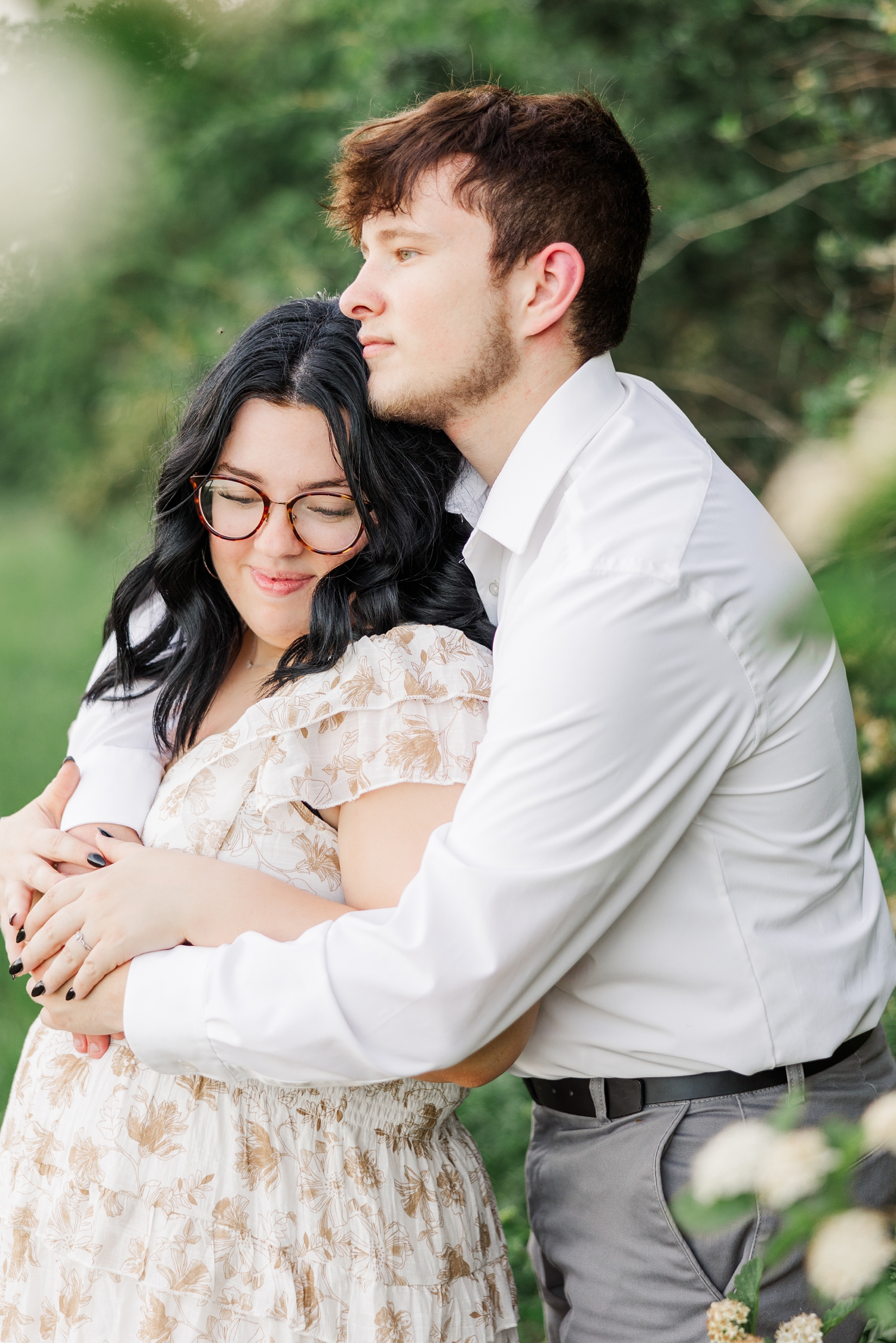 Brandon embraces Kylie from behind among white floral bushes at Water's Edge Nature Center | CB Studio
