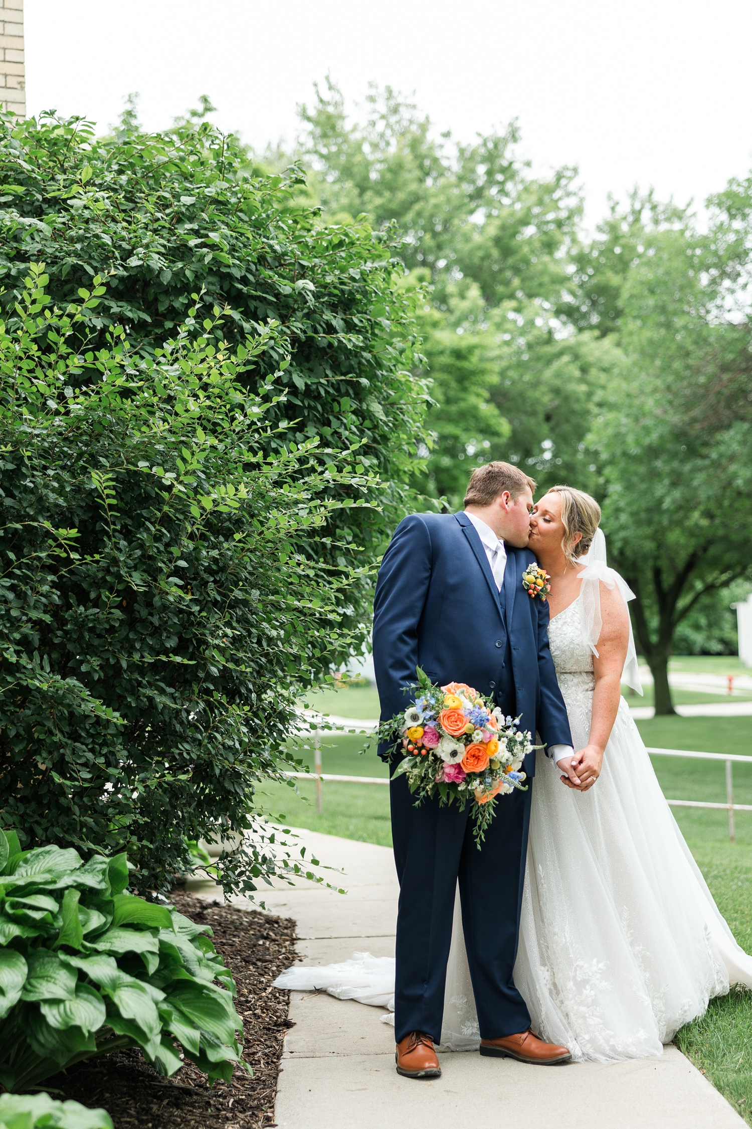 Shelby and Taylor share a kiss on a sidewalk on the backside of St. John the Baptist Catholic Church in Bancroft, IA | CB Studio