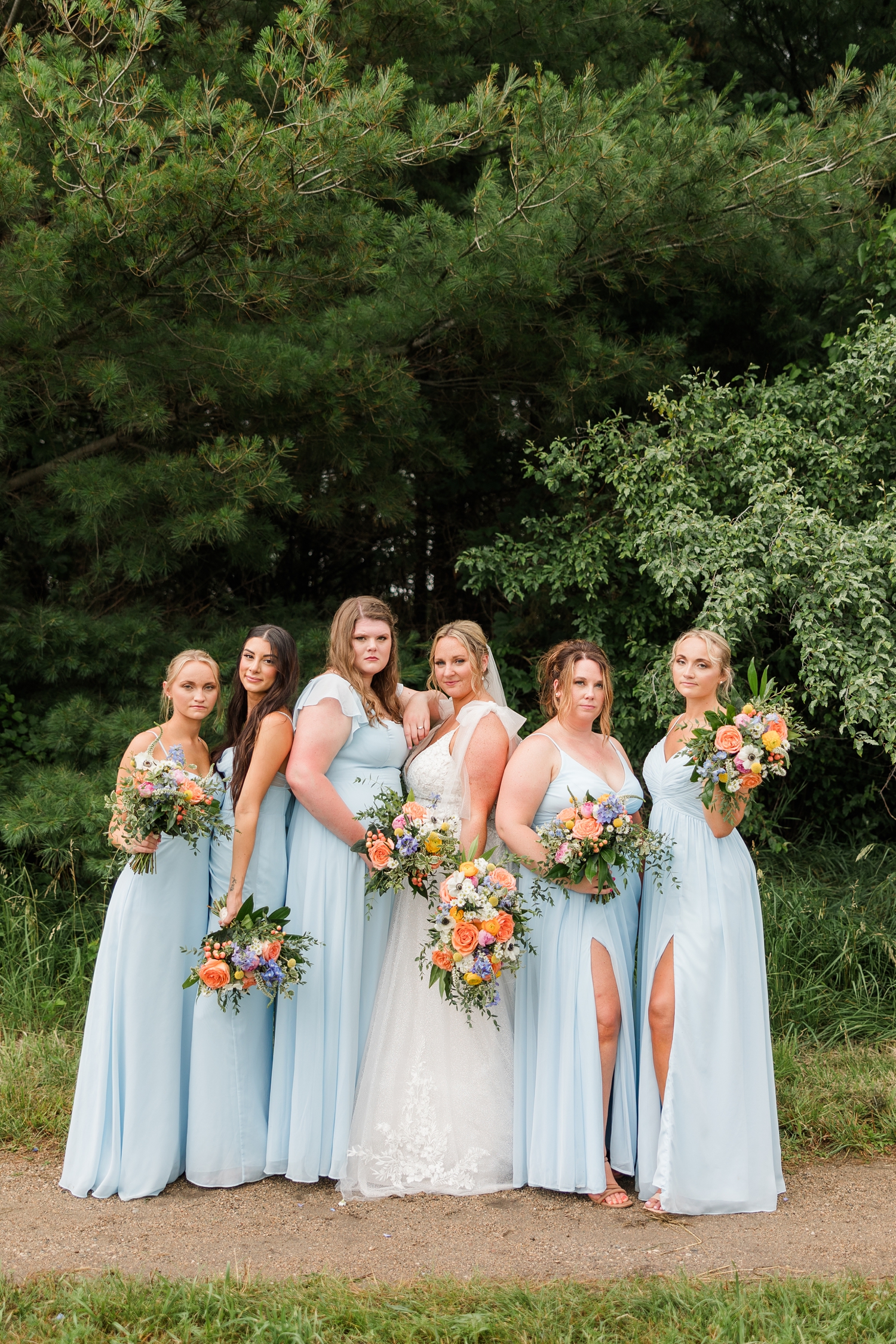 Shelby model poses with her bridesmaids wearing sky blue and holding mixed bouquets of corals, blues, whites and yellows at Water's Edge Nature Center | CB Studio