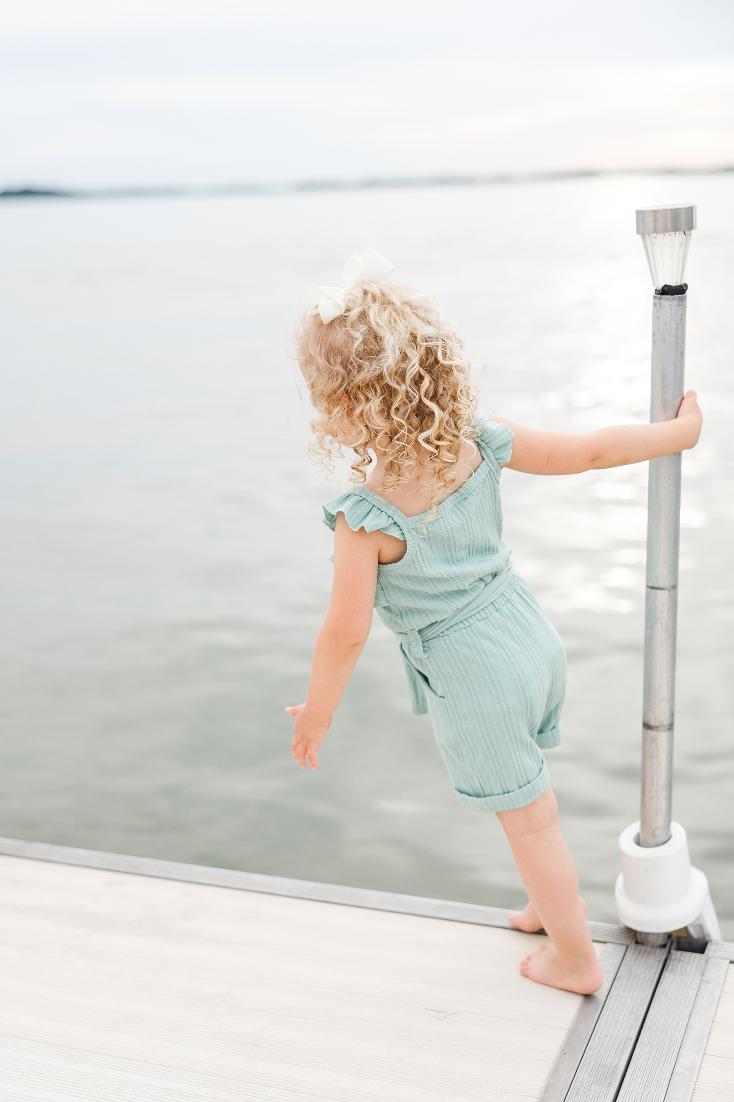 Little Lydia swings around a small light pole attached to a dock on Clear Lake, IA with the lake and sunset behind her | CB Studio