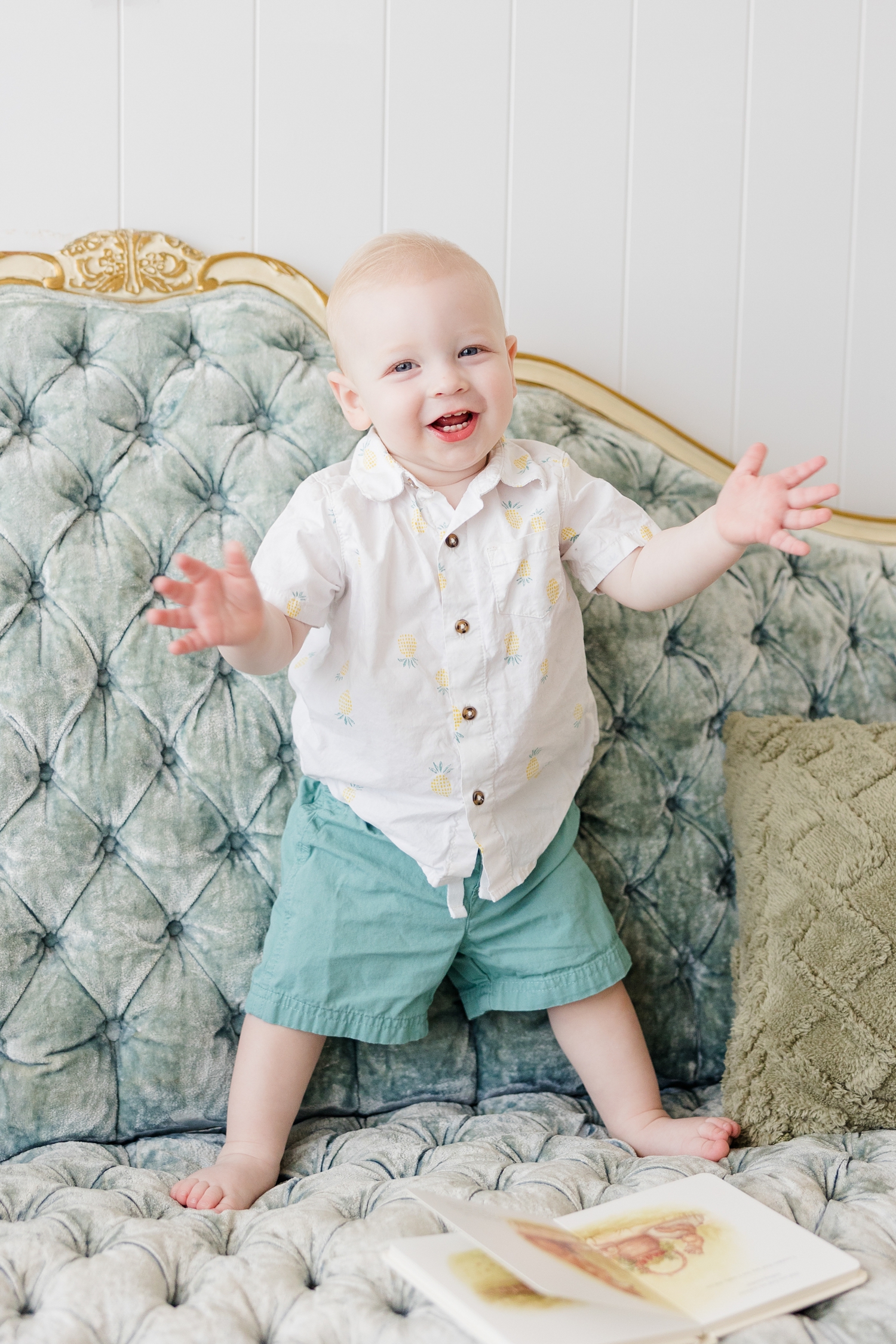 Baby Jonah stands on a blue, tufted, Victorian style couch while clapping his hands | CB Studio