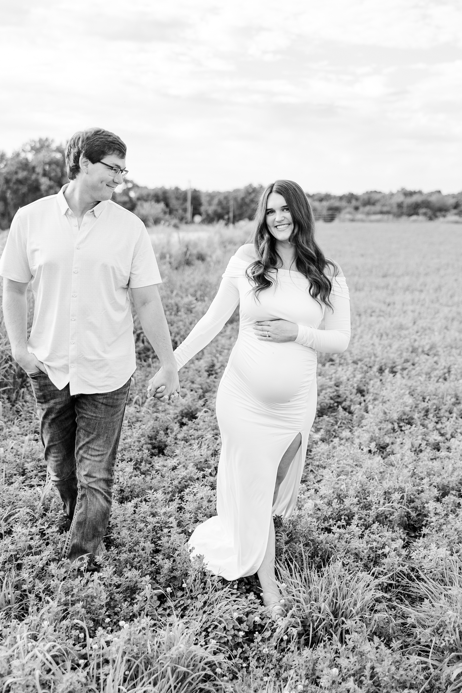 Brady and Jenna walk through an alfalfa field hand in hand as Jenna has one hand on her pregnant belly | CB Studio