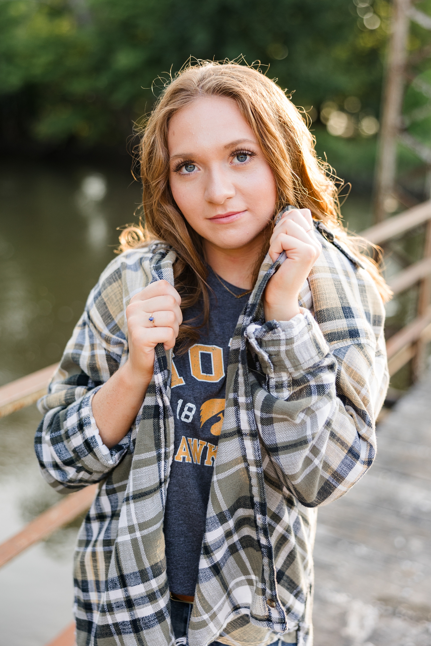 Izzie cups her flannel shirt around her face as she stands on a rustic metal bridge | CB Studio